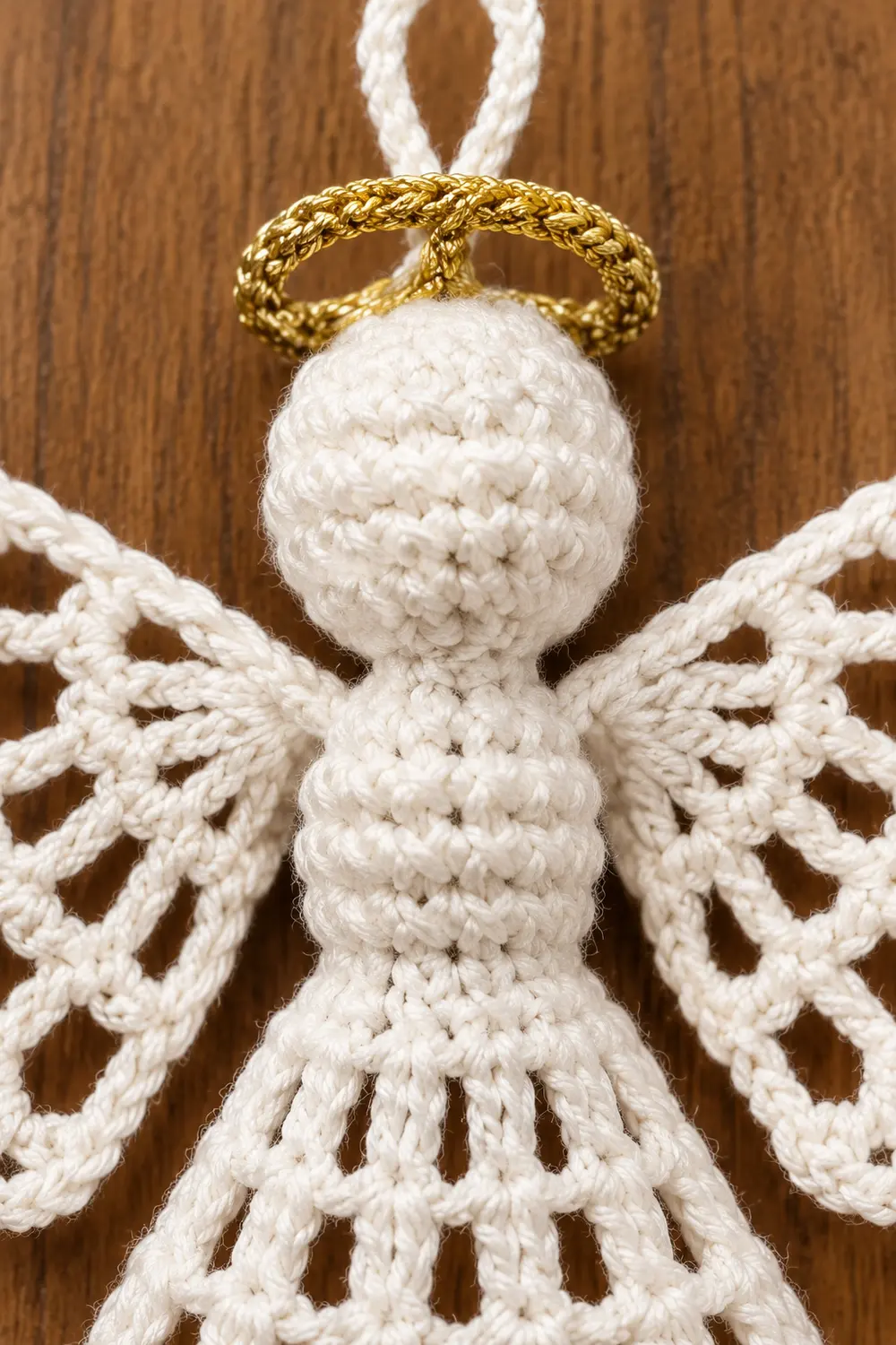 Handmade macramé angel ornament with white rope body, golden halo, and braided wings on wooden background.