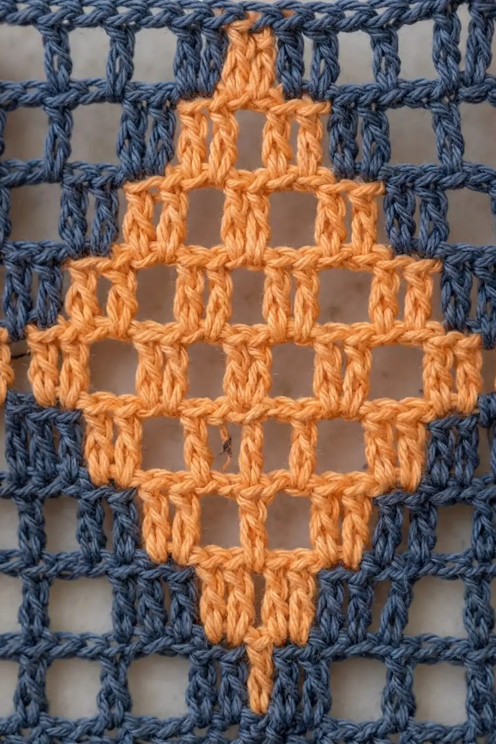 Orange cross motif stitched in crochet on a blue gridded background with visible yarn texture.