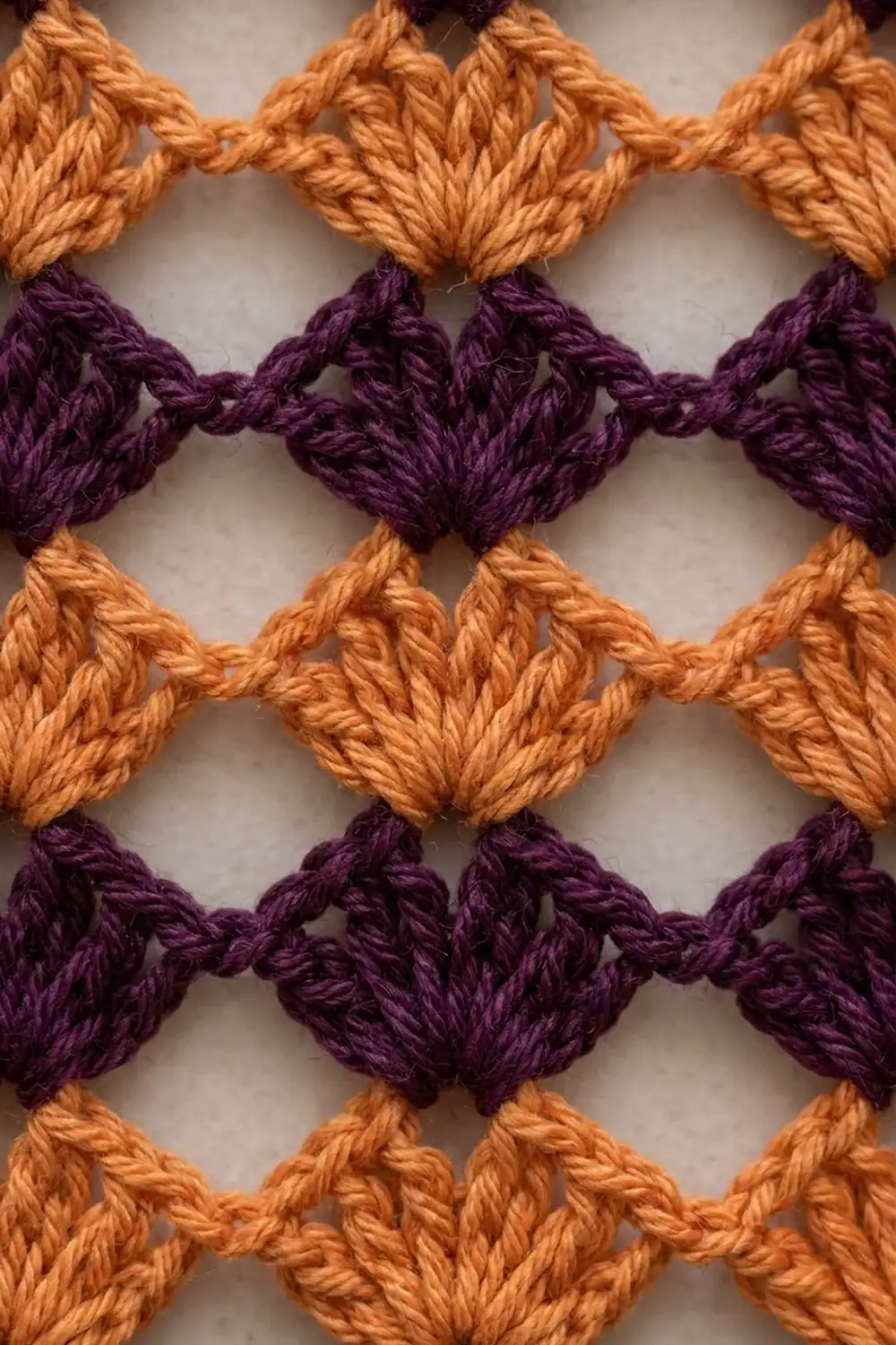 Textured crochet pattern featuring interlocking diamonds in golden orange and deep purple yarn strands.