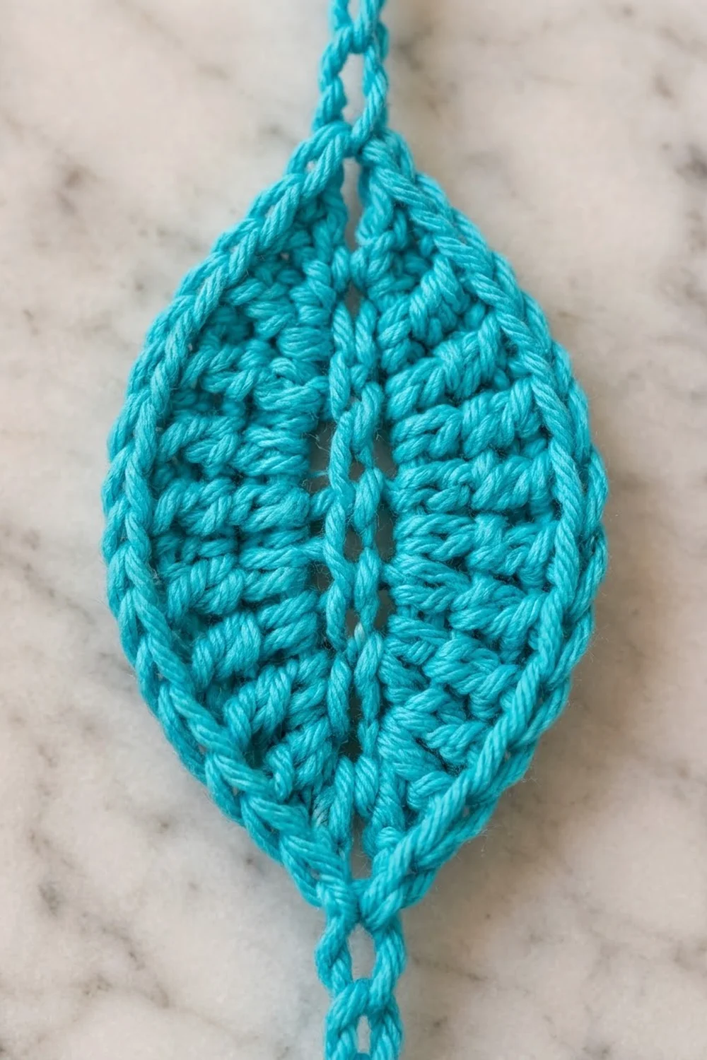 Turquoise crocheted teardrop ornament with intricate openwork pattern, hanging against speckled marble.