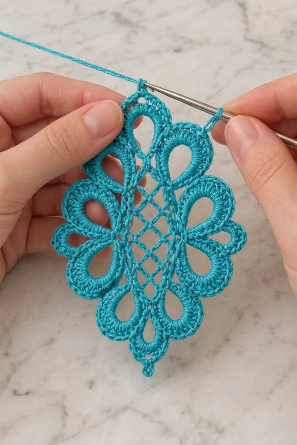 Hands holding a turquoise crocheted snowflake motif with open lace work on a marble background.