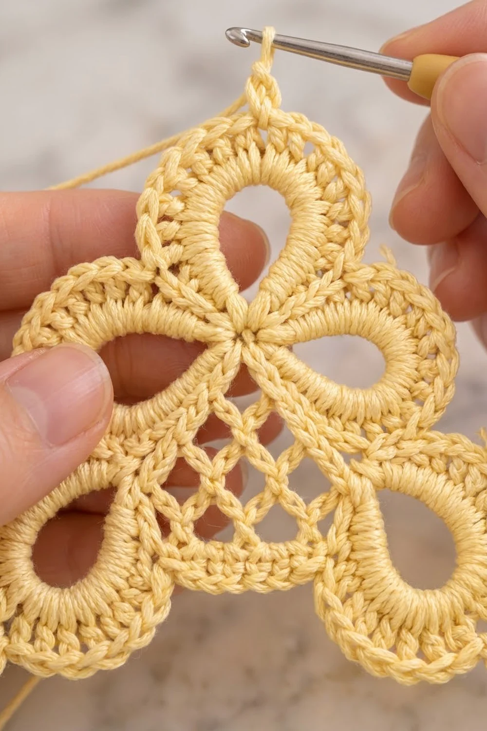 Close-up of a cream-colored crocheted lace motif being worked with a silver crochet hook.