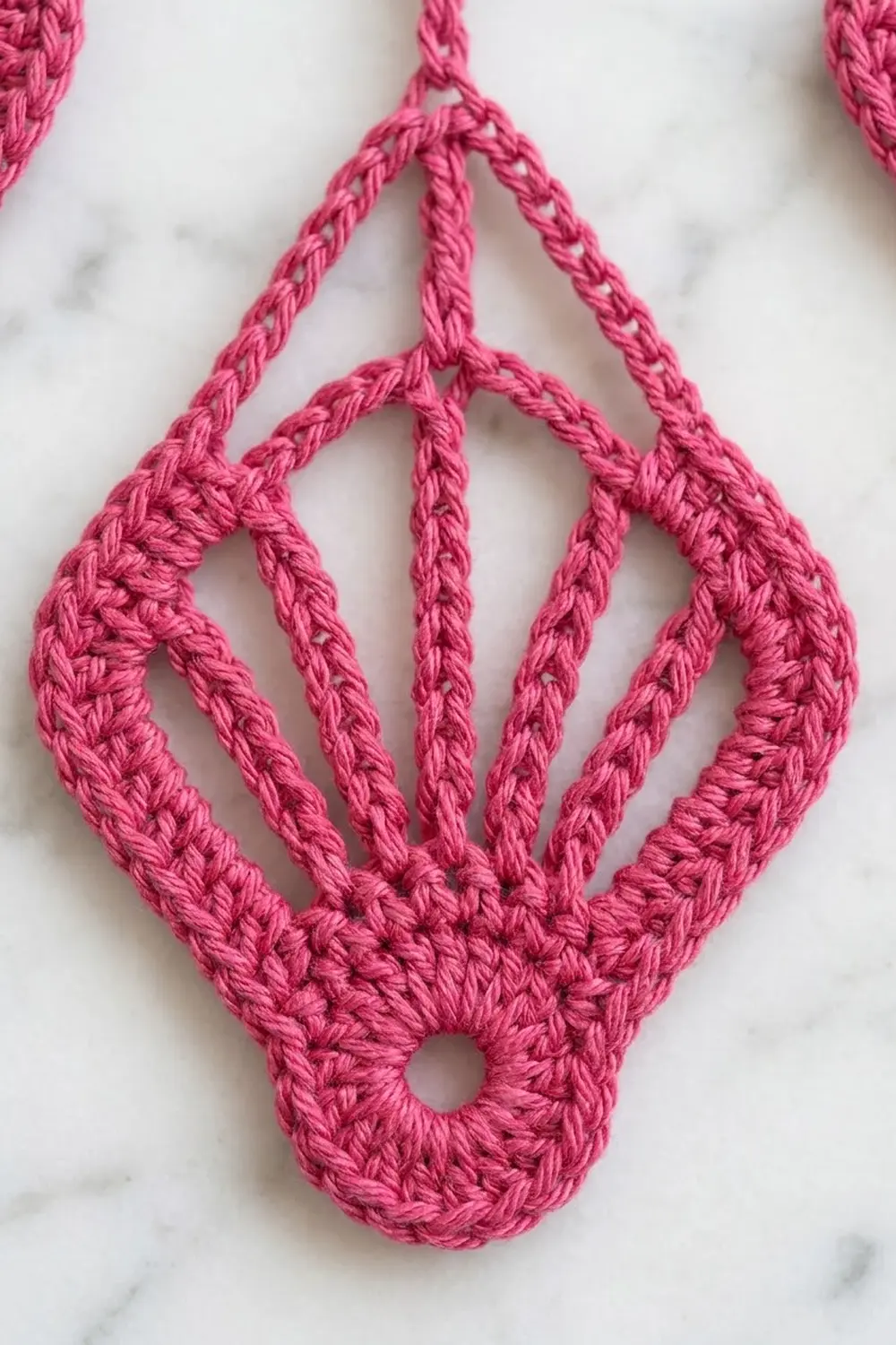 Close-up of bright pink crocheted diamond shape with visible texture on white marble background.