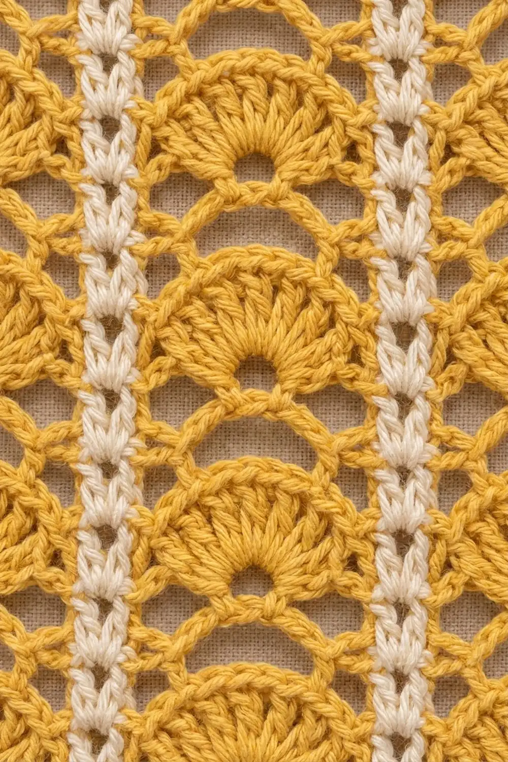 Close-up of golden yellow and cream yarn crochet with repeating openwork oval stitch pattern.