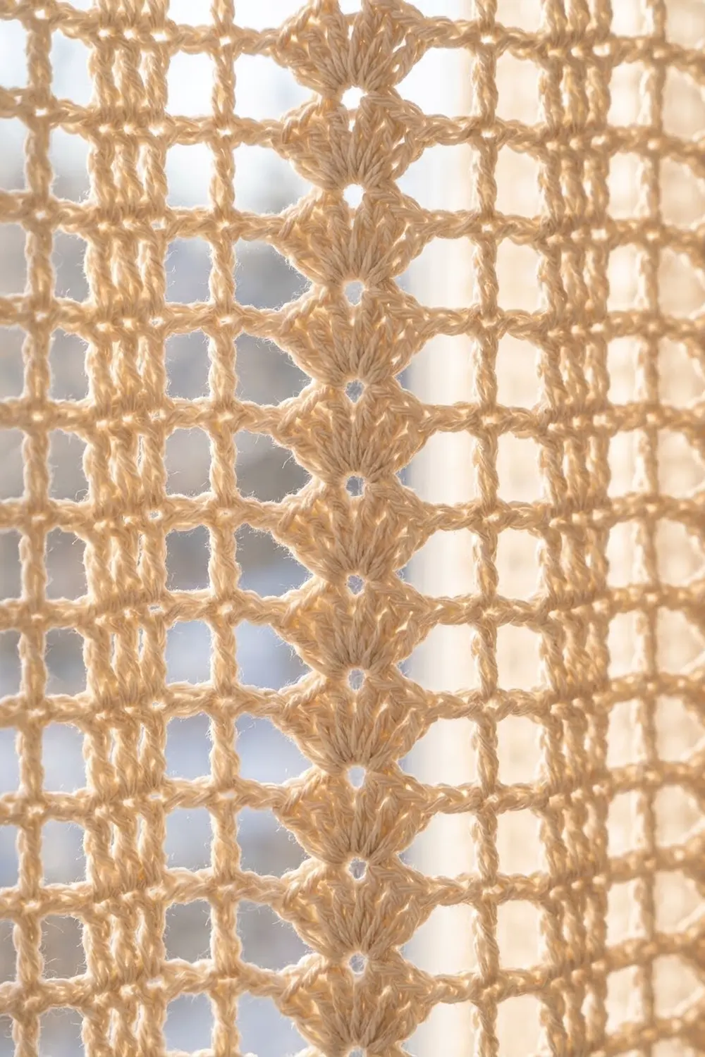 Close-up of tan crocheted textile featuring geometric diamond pattern with decorative knotted nodes and open-work design.