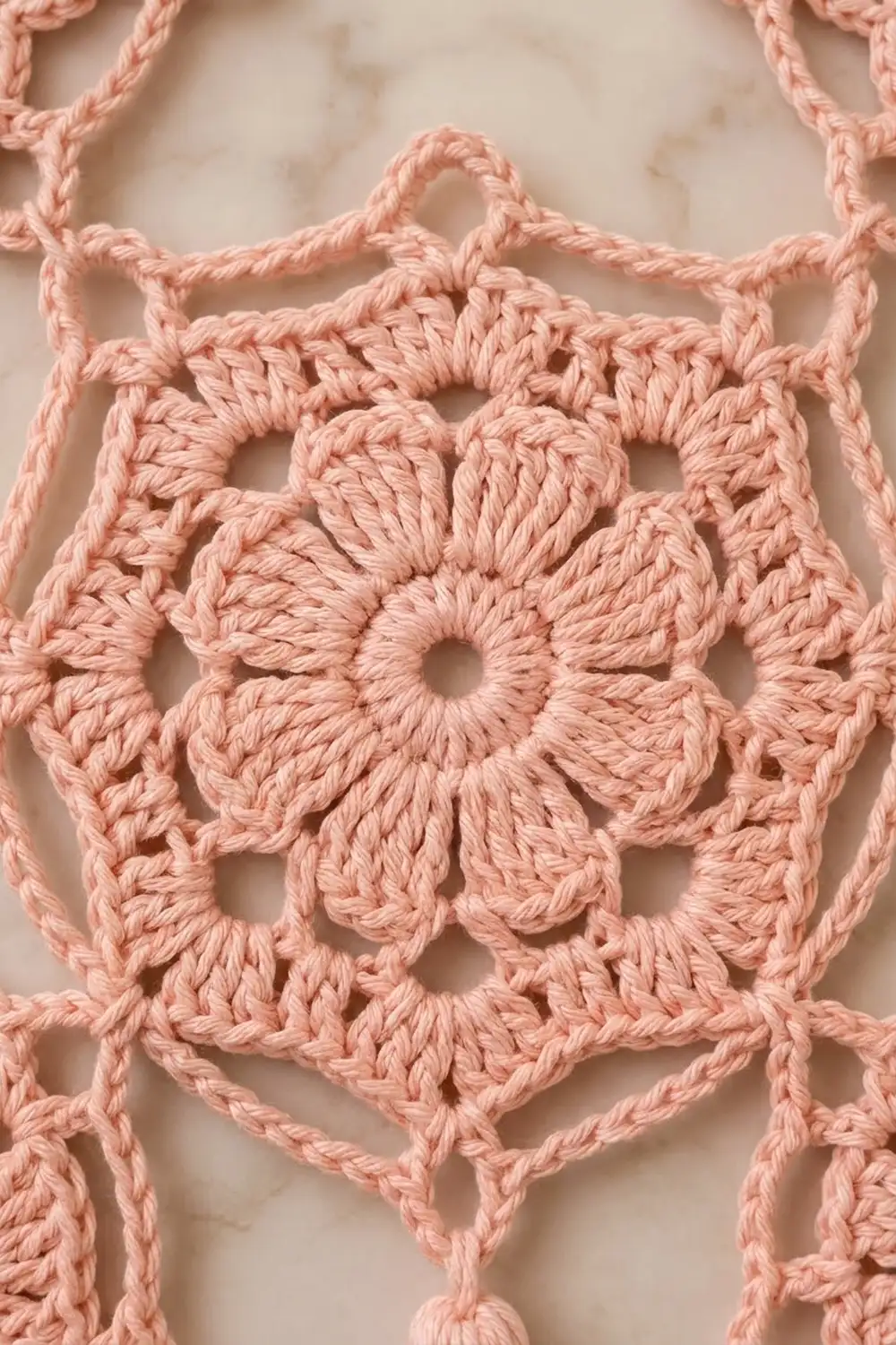 Close-up of pink crochet featuring a flower medallion with delicate openwork and intricate stitching on cream background.