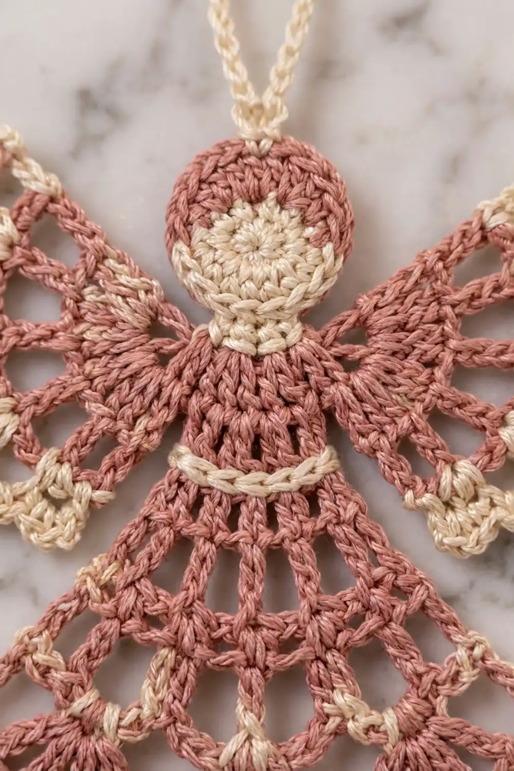 Crocheted doll with rosy-pink body, cream head, limbs, and band details, showing precise yarn stitching.