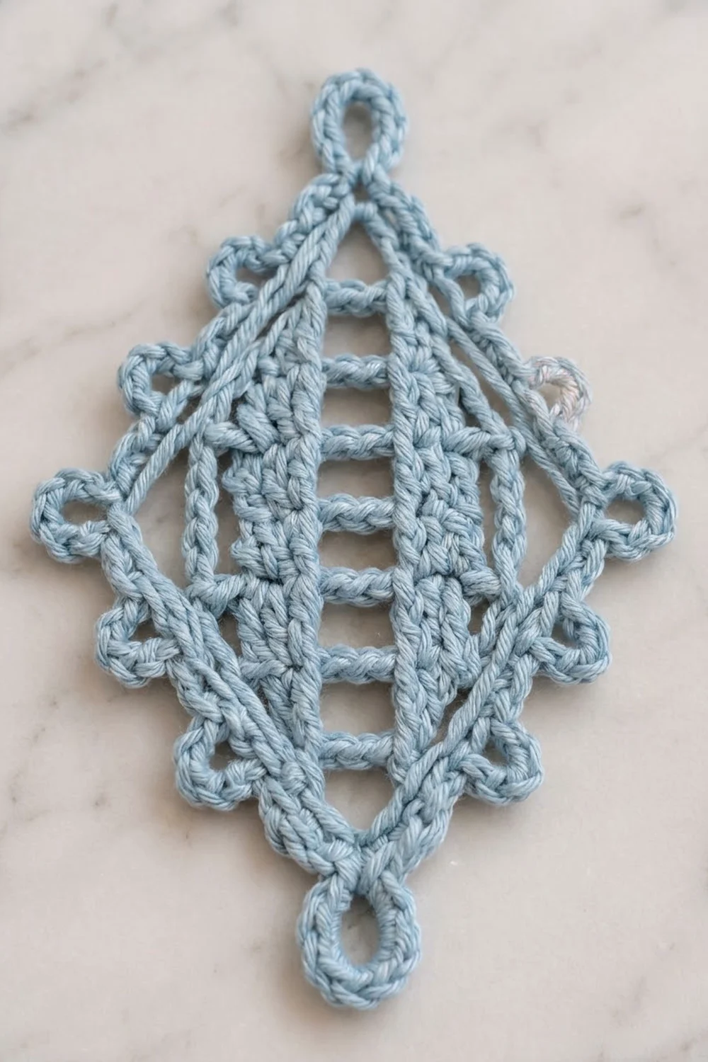 Light blue crocheted snowflake ornament with geometric diamond pattern on a white marble background.