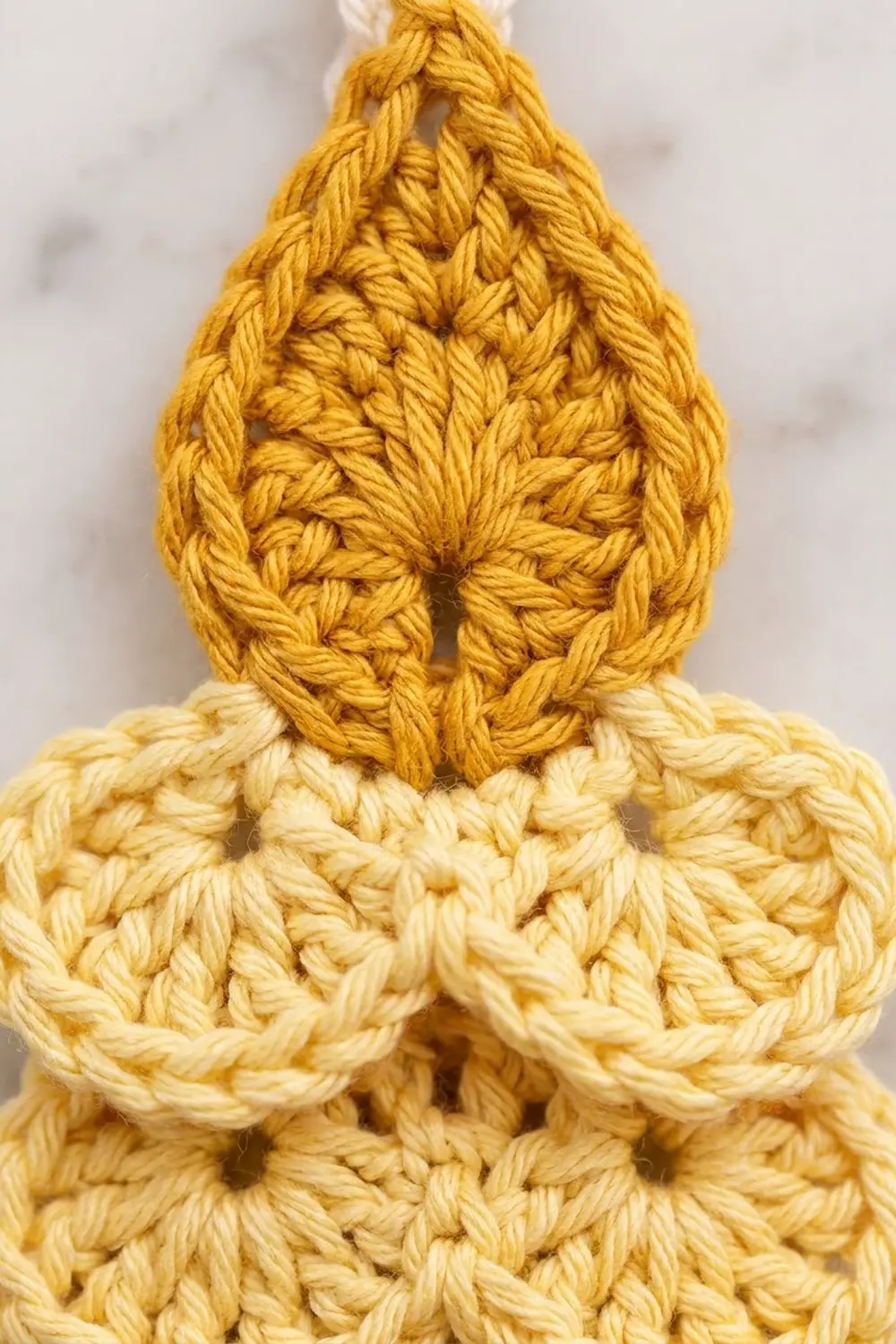 Closeup of mustard-yellow crocheted teardrop with cream base, showcasing detailed stitch texture on a soft neutral background.