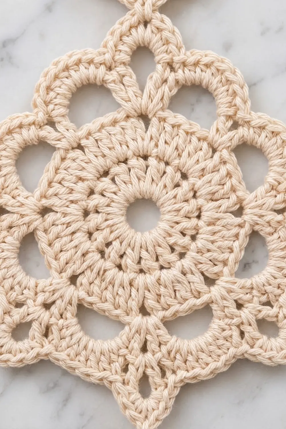 Cream-colored crocheted medallion with intricate lace pattern displayed on white marble surface.