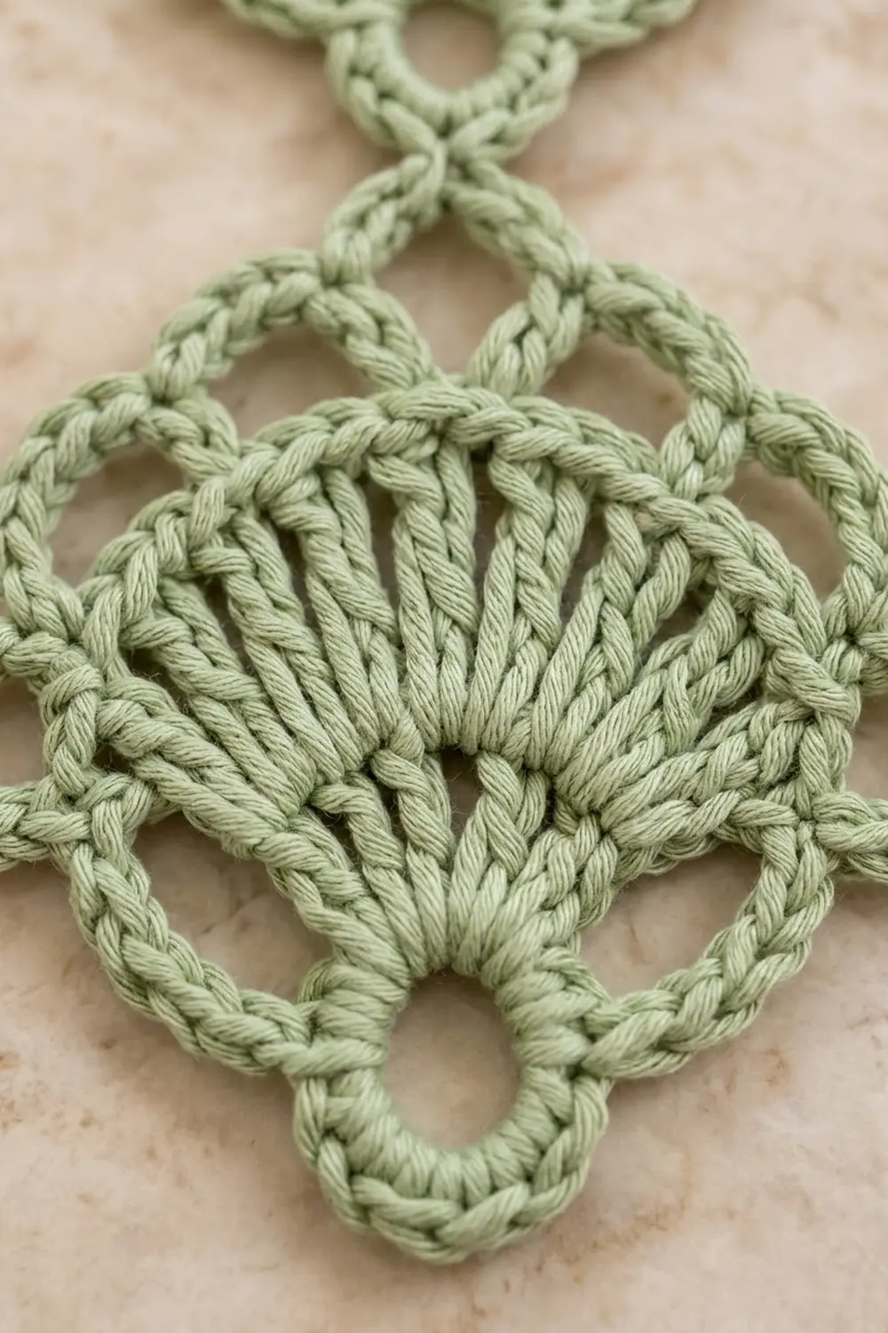 Sage green crochet lace with intricate braided stitching forming geometric diamond motifs, displayed on a neutral beige background.