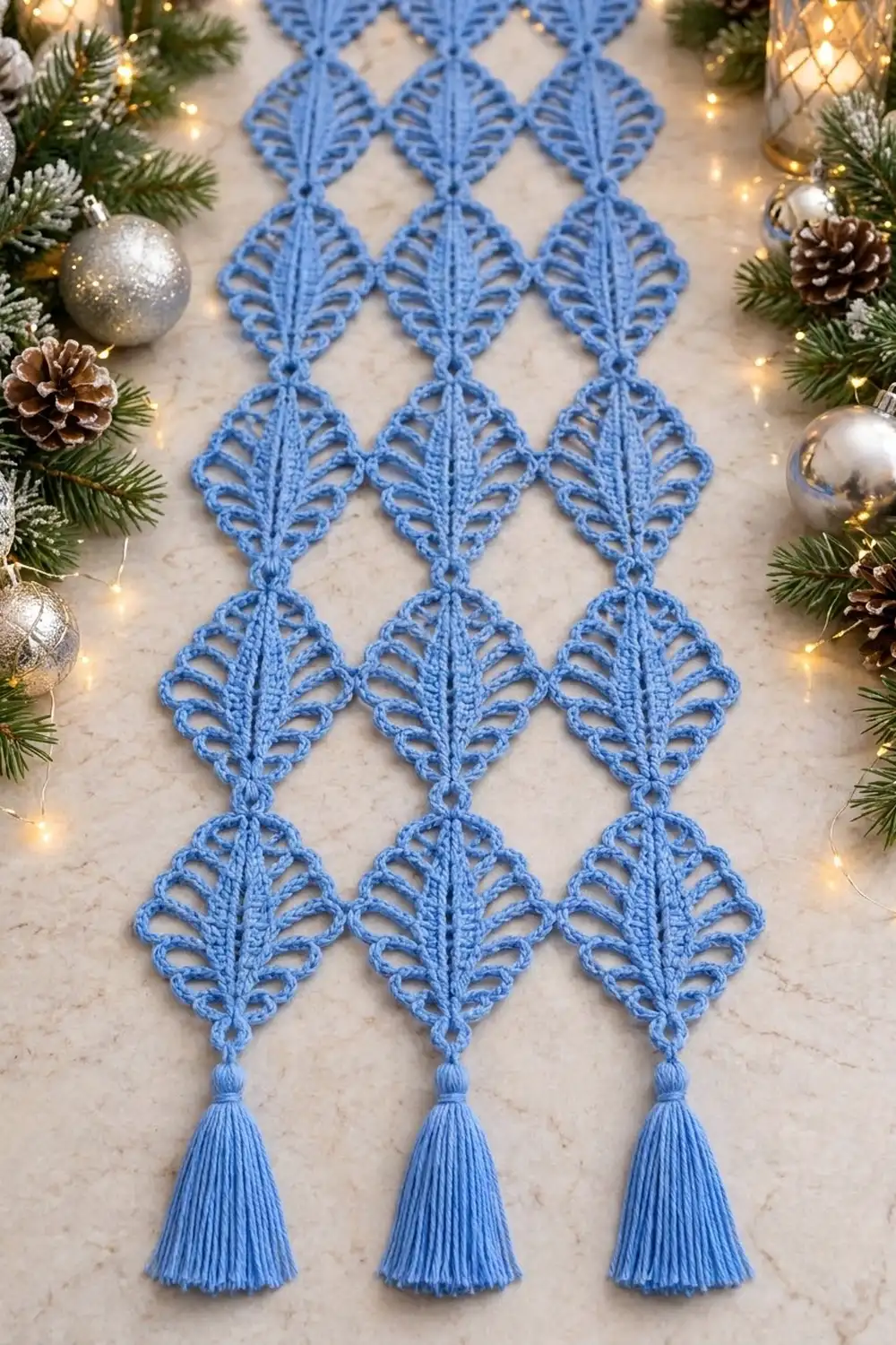 Intricate blue lace diamond motifs with tassels displayed on marble, framed by evergreen, ornaments, and golden lights.