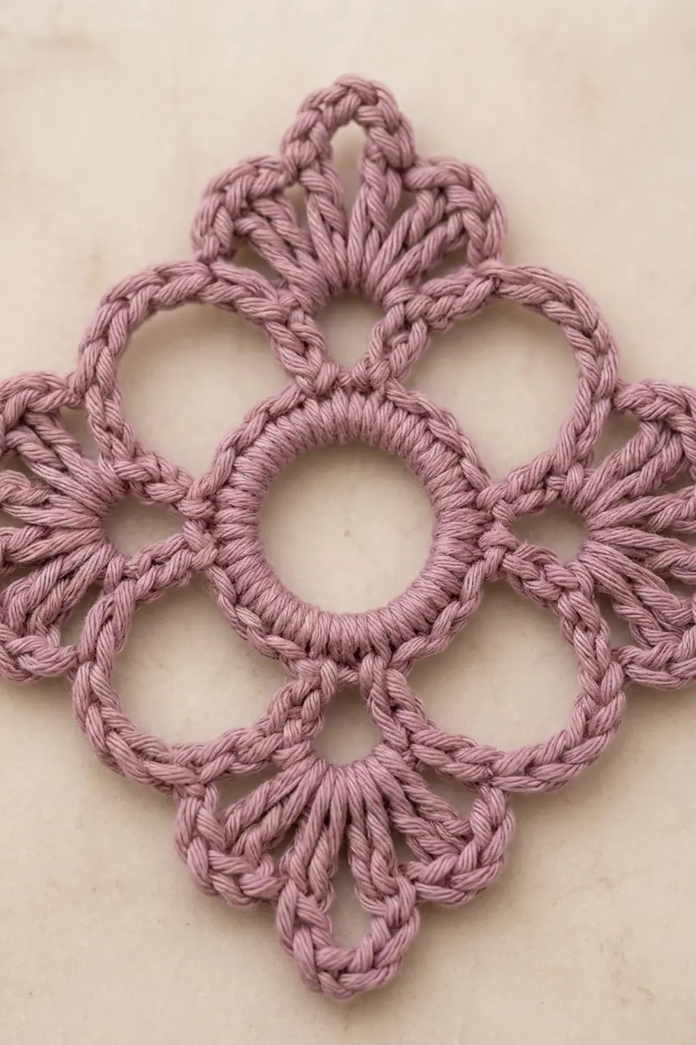 Dusty pink crocheted lace featuring interlocking circular rings that form a delicate flower-like medallion pattern on a neutral background.