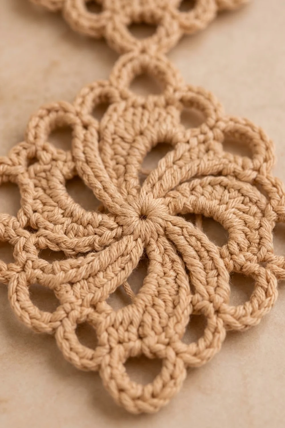 Cream-colored crocheted lace doily with intricate openwork loops and knots on a soft beige background.