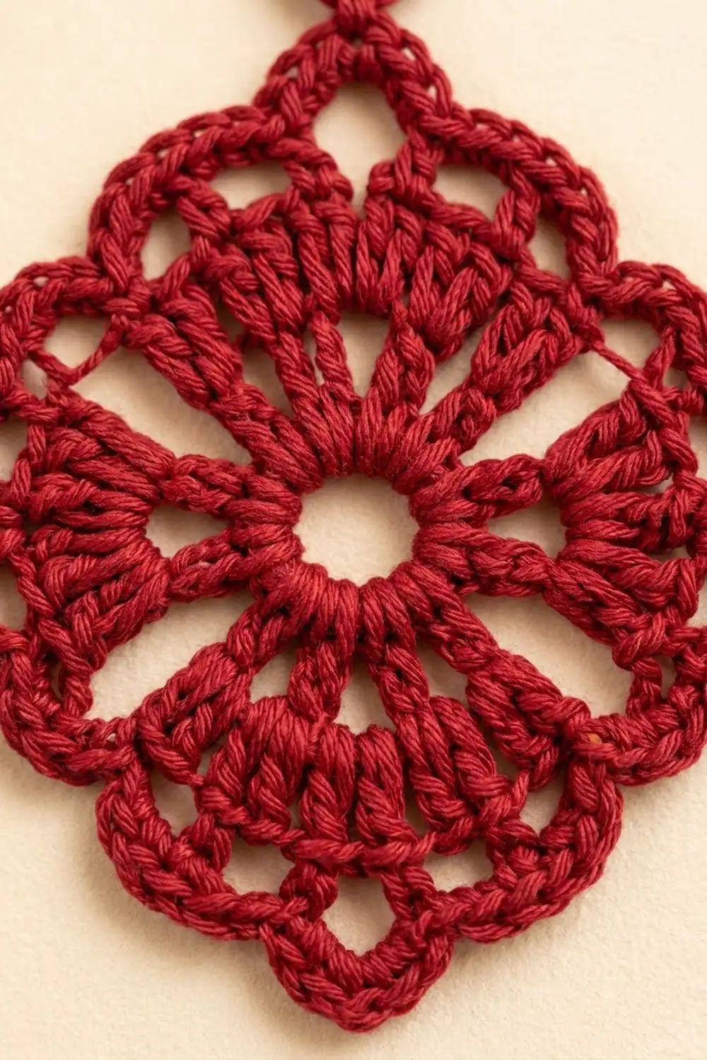 Detailed close-up of a symmetrical red crocheted doily with connected loops forming a four-pointed star pattern on cream background.