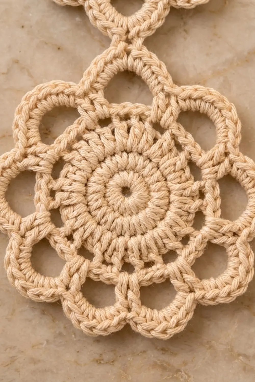 Intricate cream crochet motif featuring geometric patterns and a decorative flower center on a neutral beige background.