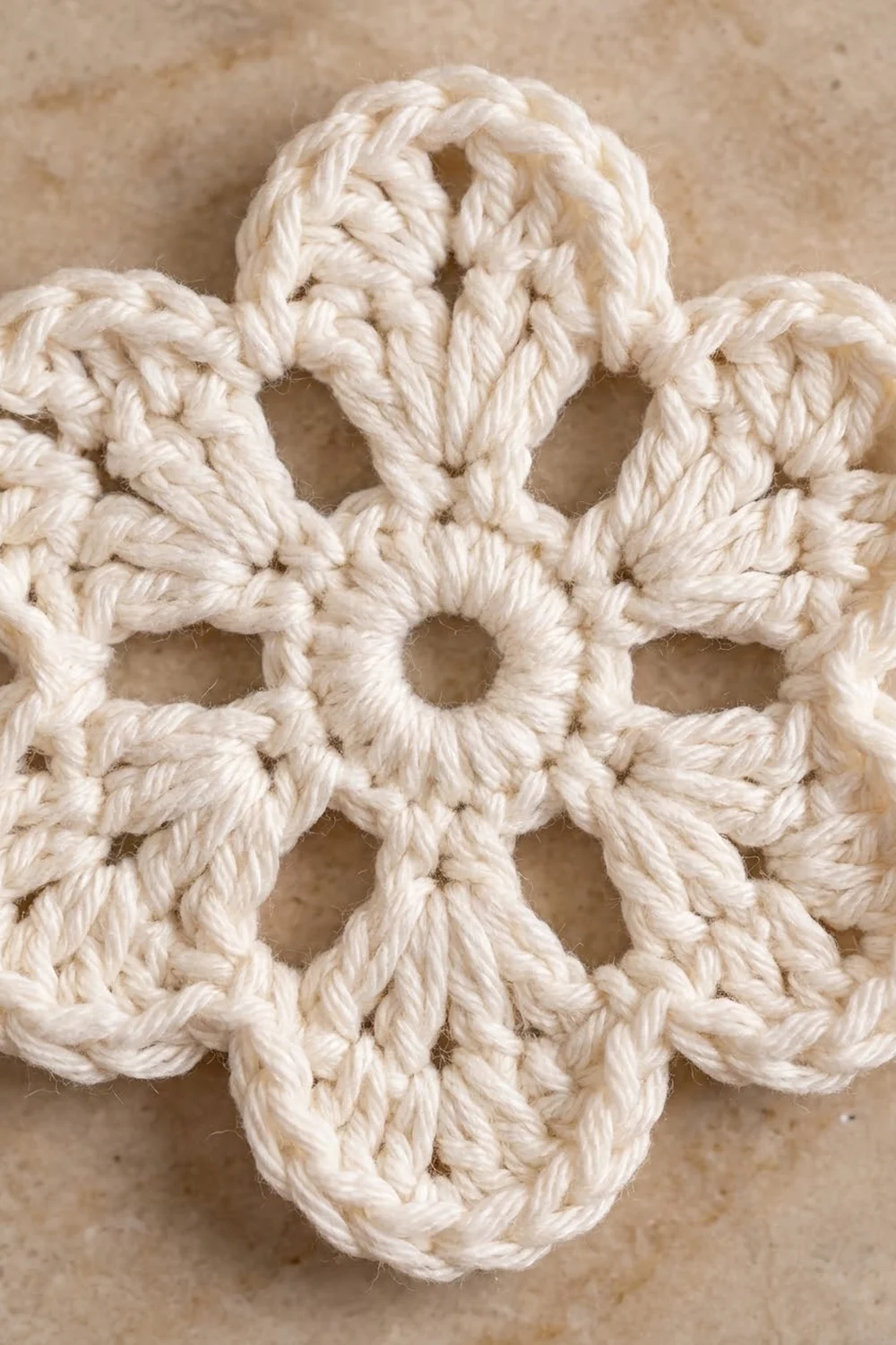 A delicate cream crochet square with an ornate geometric pattern on a neutral concrete-textured background.
