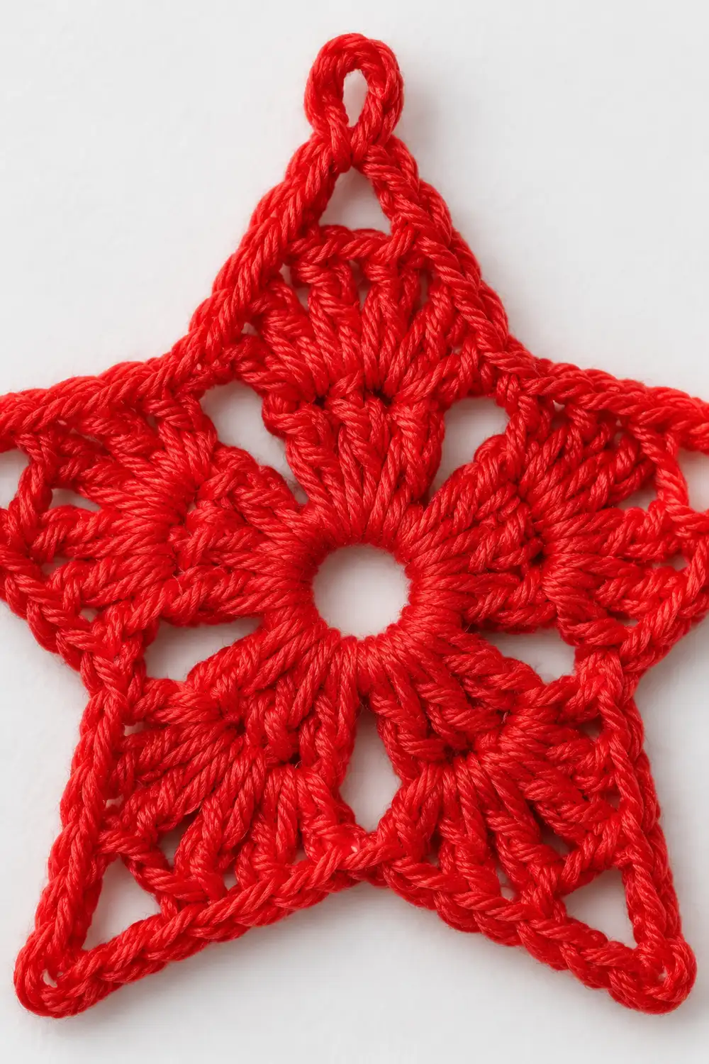 A bright red crocheted star ornament with a loop for hanging against a white background.