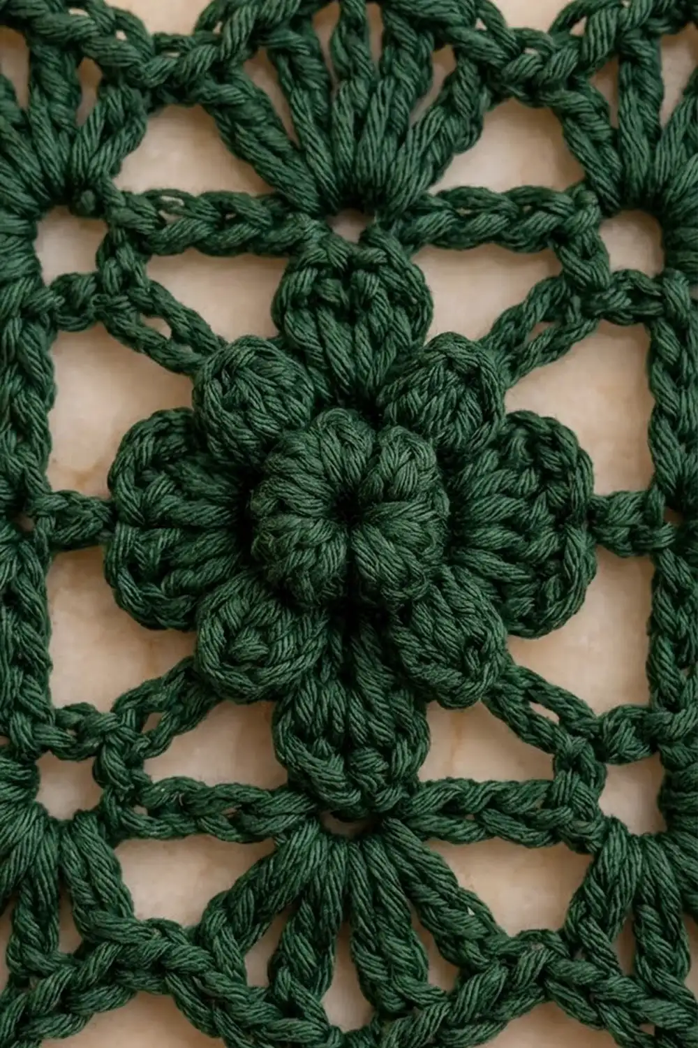 Dark green crocheted yarn with interlocking flower motifs forming a repeating geometric pattern on cream background.