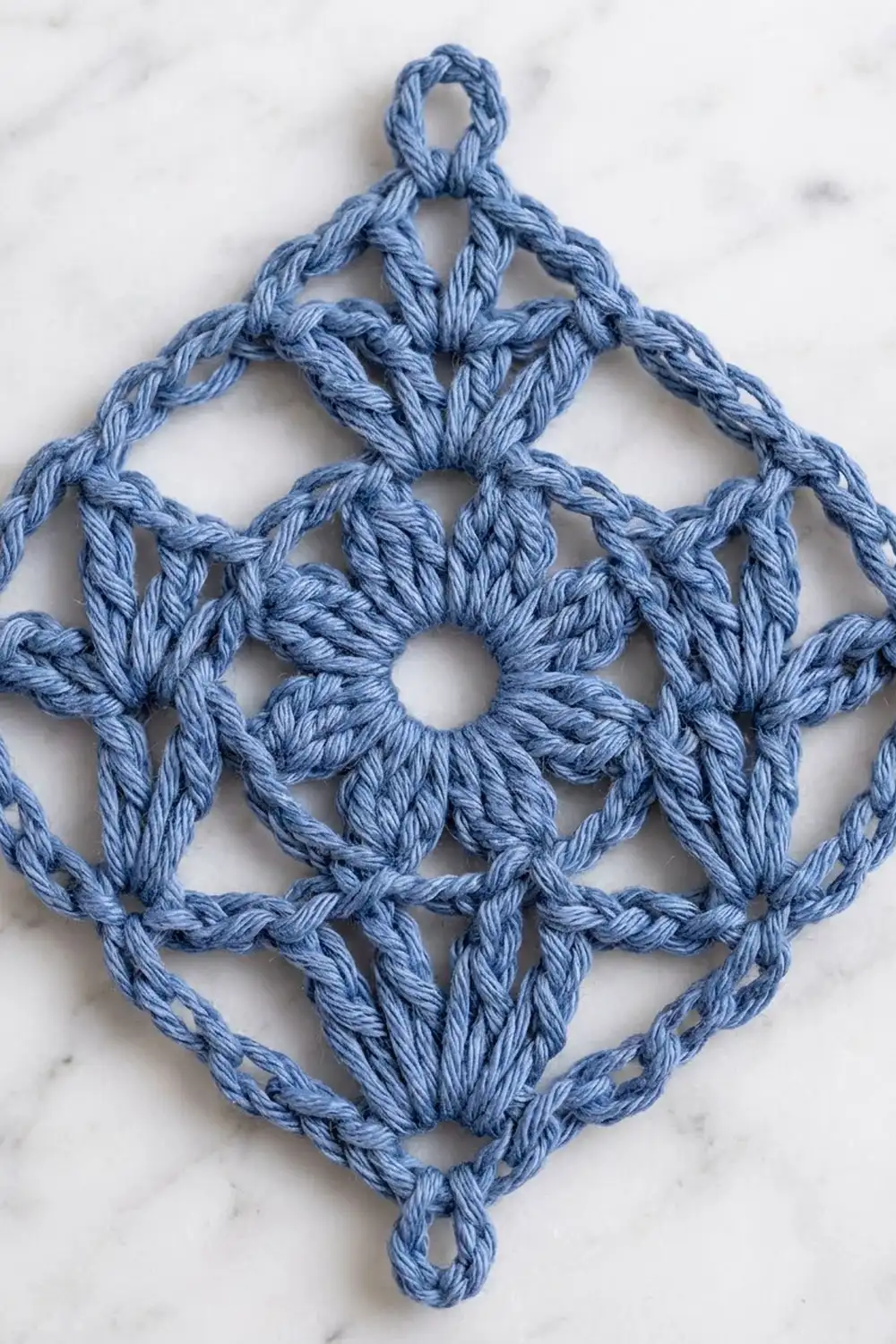 Light blue crochet ornament with geometric openwork pattern displayed on a white marble background.
