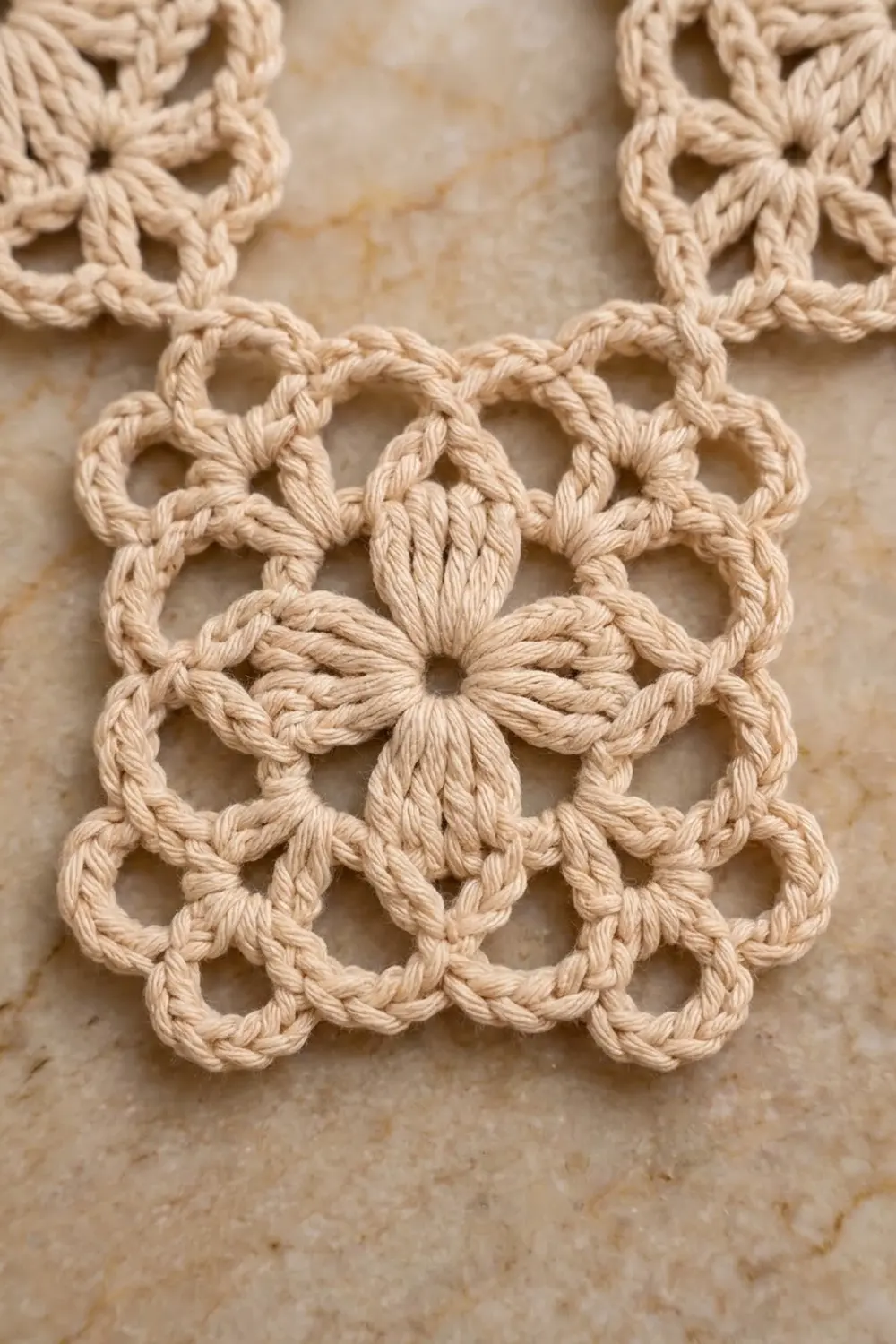 Close-up of cream crochet motif with lacework pattern and central flower detail on neutral background.