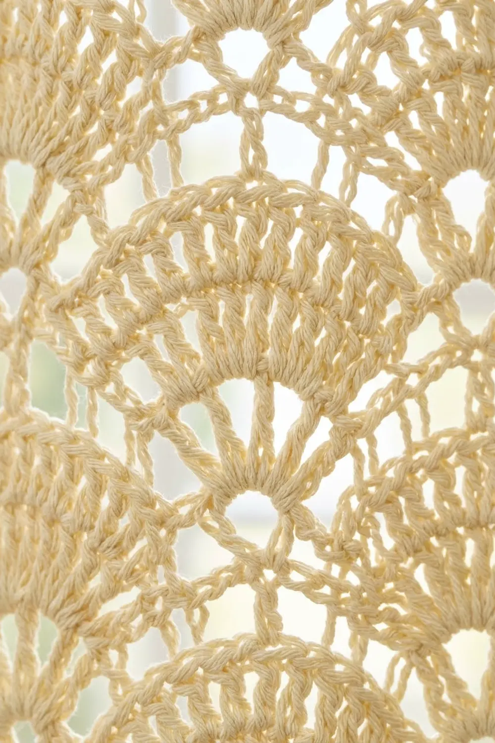 Beige macramé or crocheted cord arranged in geometric knotted pattern with open spaces and backlit.