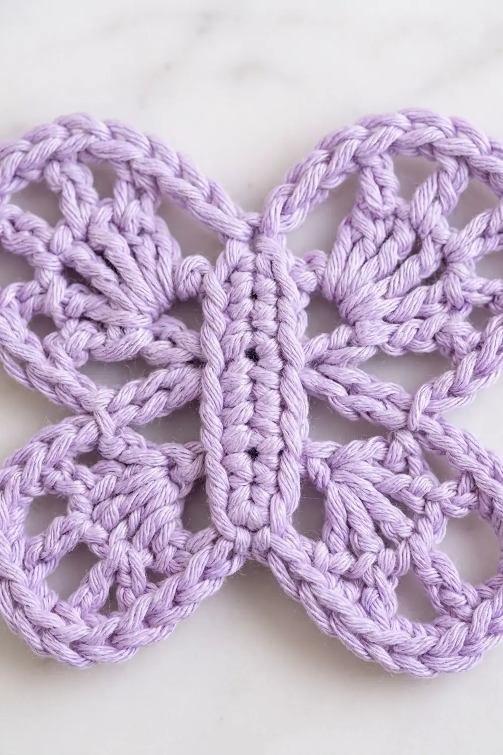 Detailed close-up of a lavender crocheted lace motif with an open geometric pattern against a white background.