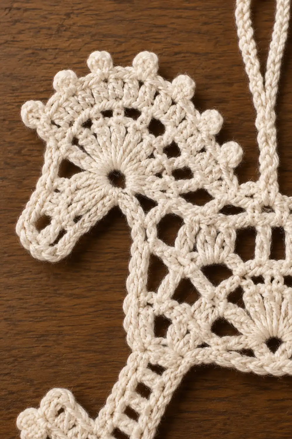 Cream-colored crocheted lace with floral motifs and picot edging displayed on a wooden surface.