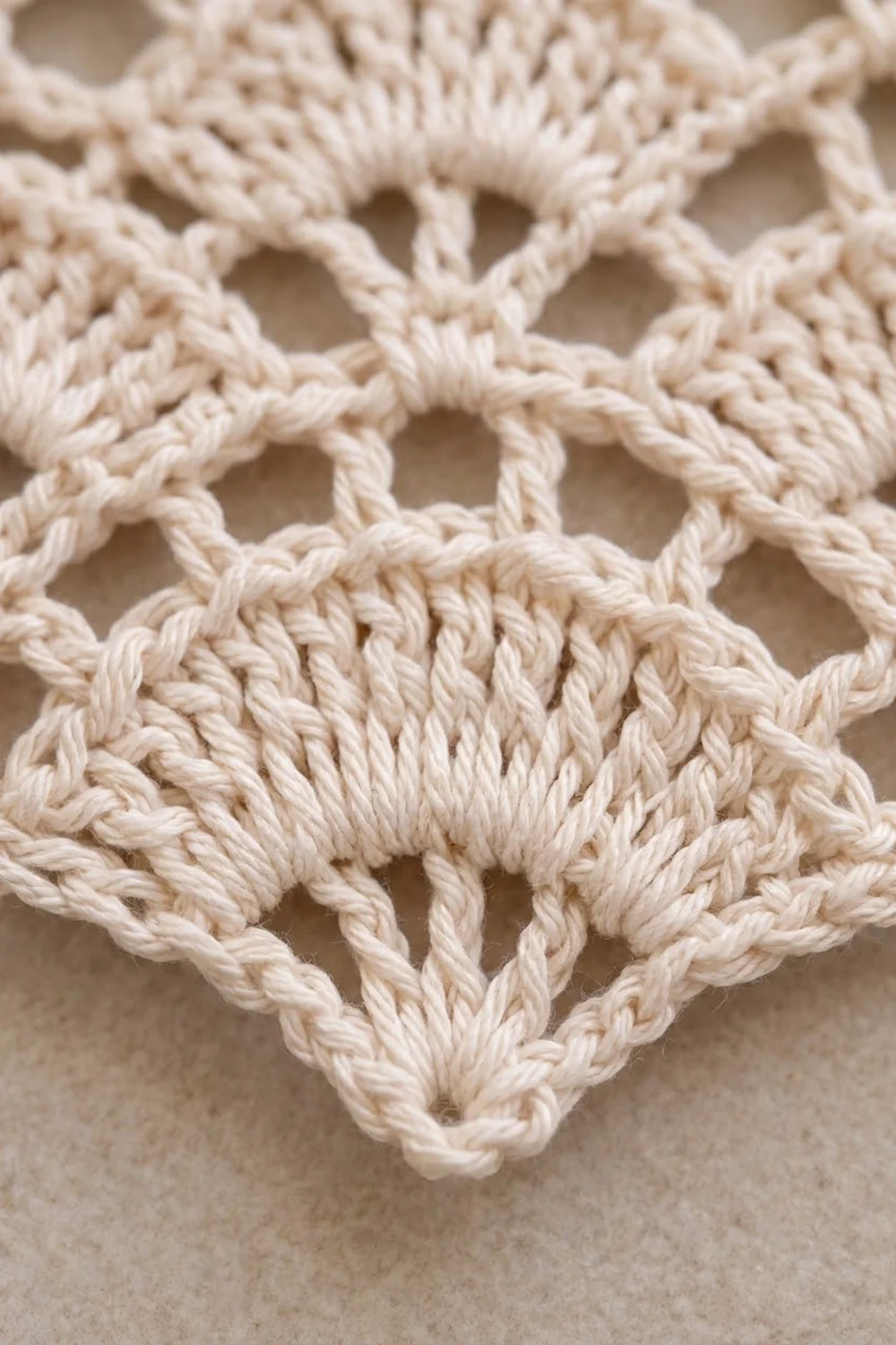 Close-up of cream cotton macramé with twisted rope knots creating an open diamond lace pattern.