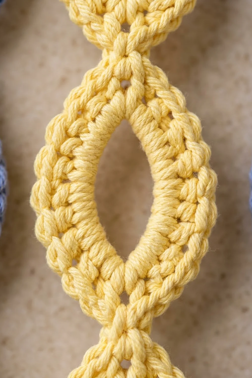 Bright yellow crocheted chain loop with distinct stitch details against a soft, blurred neutral background.