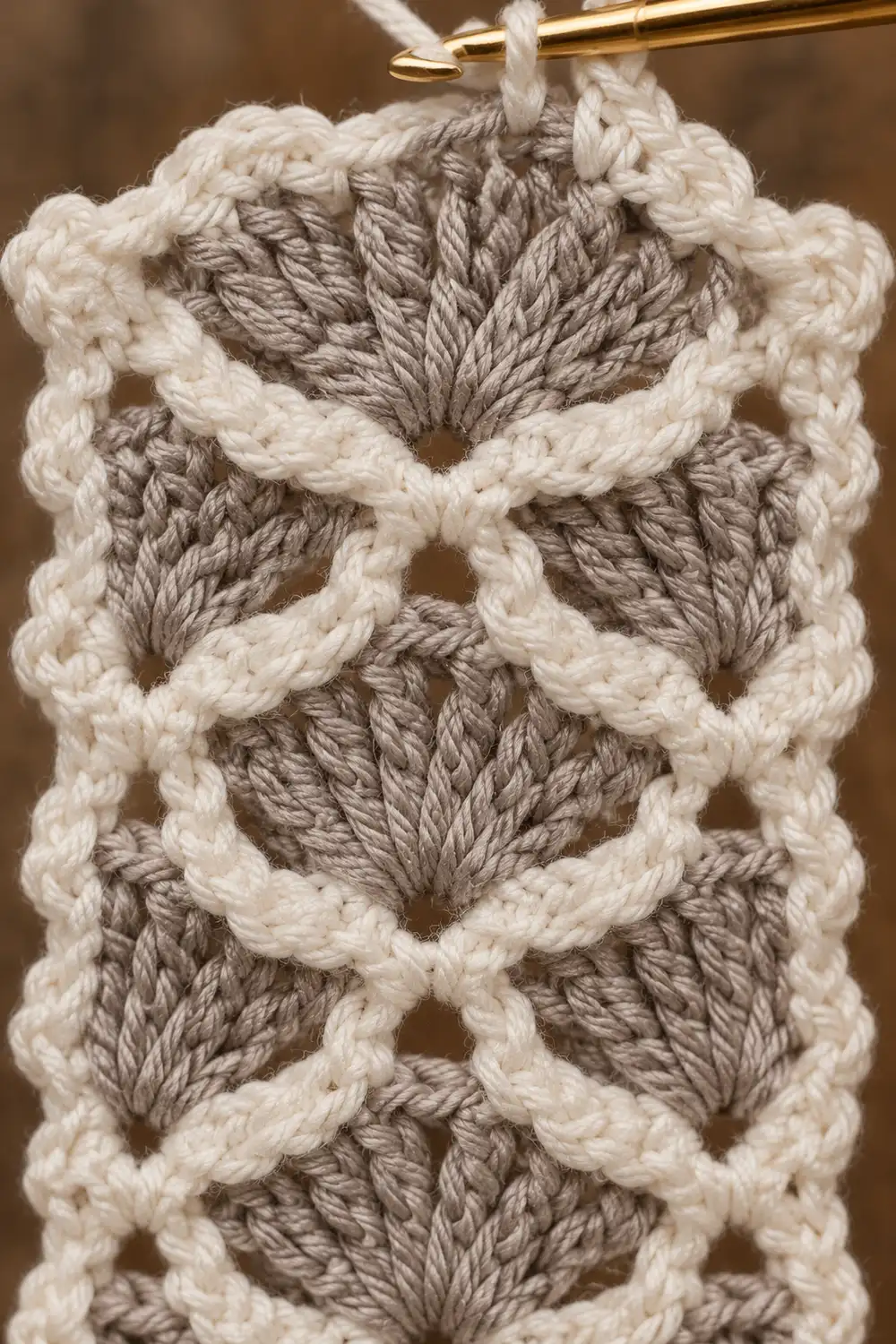 Close-up of a crocheted bookmark or hanging ornament in cream and taupe yarn showing detailed stitch pattern.