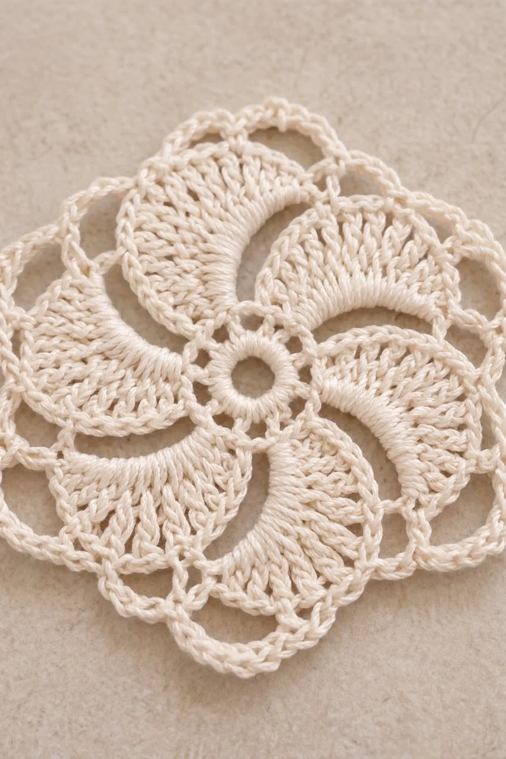 Cream-colored crocheted flower motif with intricate openwork stitching and curved petals on neutral beige background.