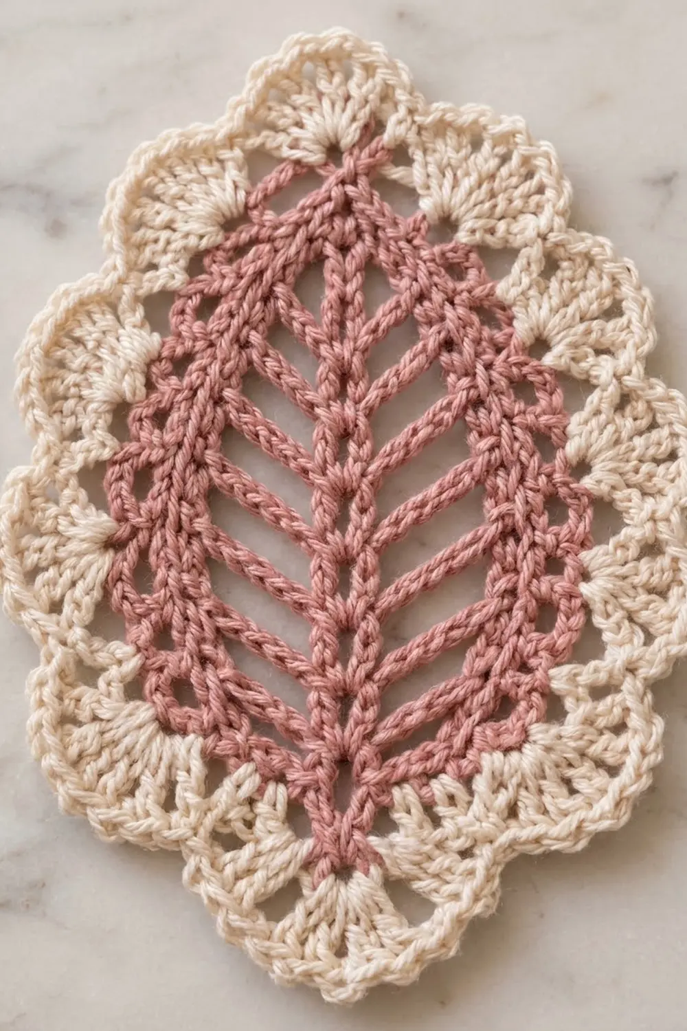 Cream and dusty pink crocheted doily with a chevron pattern center on a marble surface.