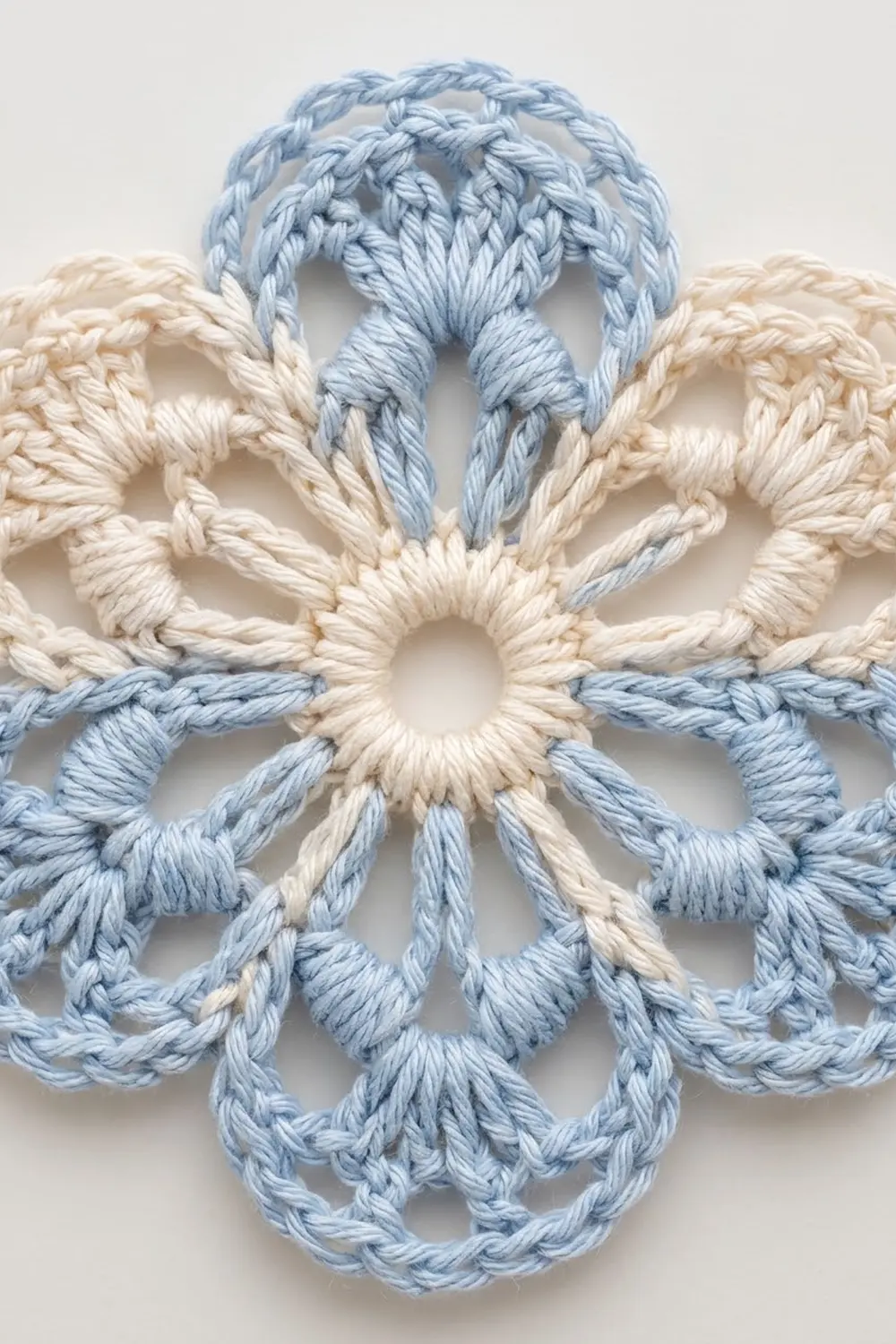 Close-up of a crocheted snowflake motif in light blue and cream yarn with intricate loop details against a neutral background.