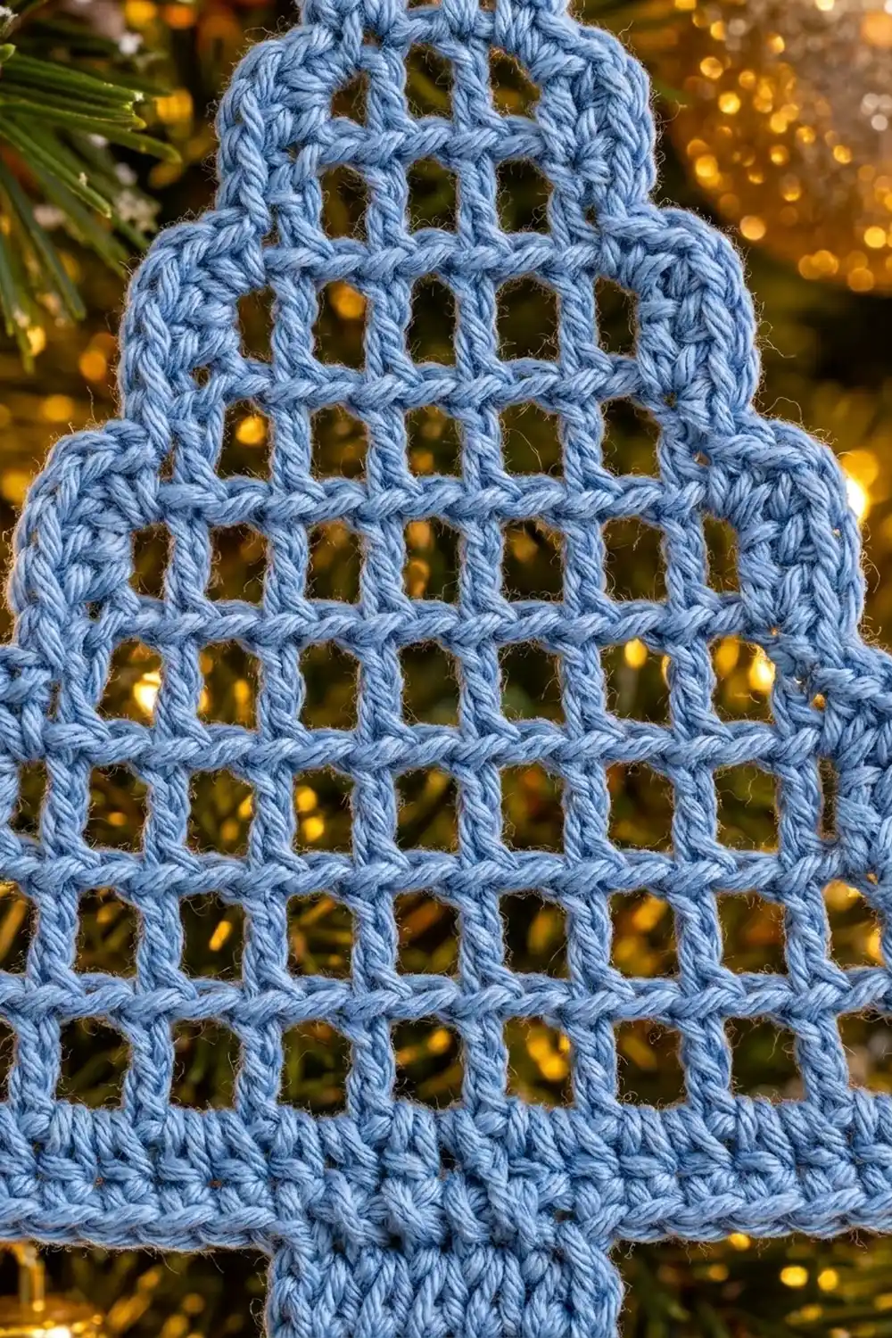 Light blue crocheted ornament with open lattice pattern, photographed against warm golden bokeh lights and green foliage.