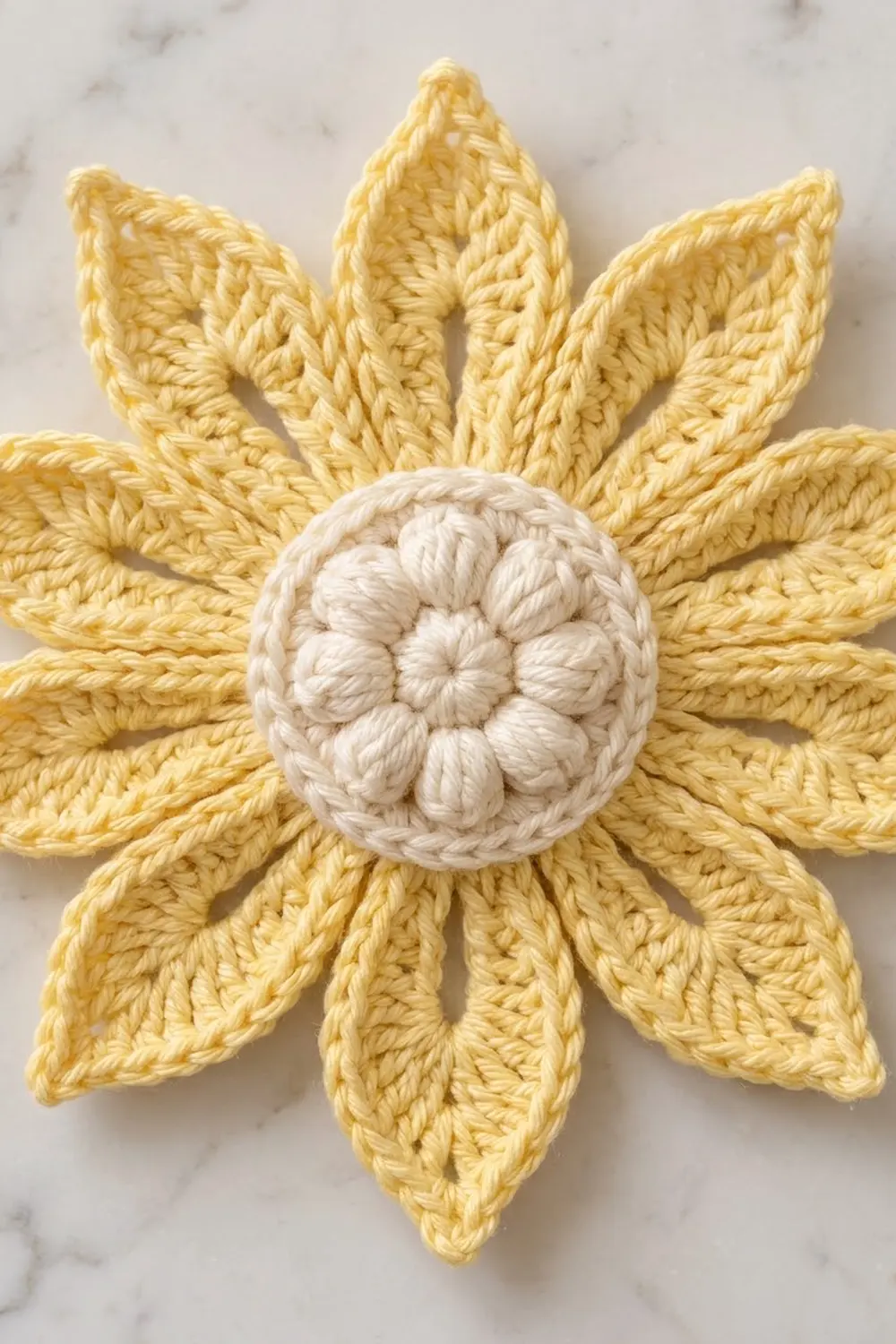 Handmade crocheted sunflower with golden yarn petals and cream-textured center detail on marble surface.