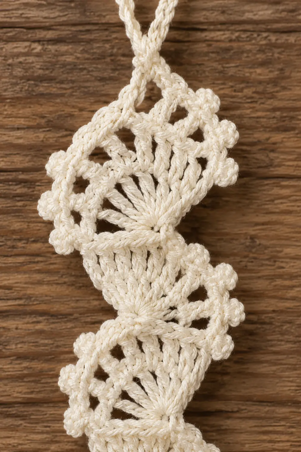 Cream-colored macramé pendant with knotted geometric patterns hanging against a wooden background.