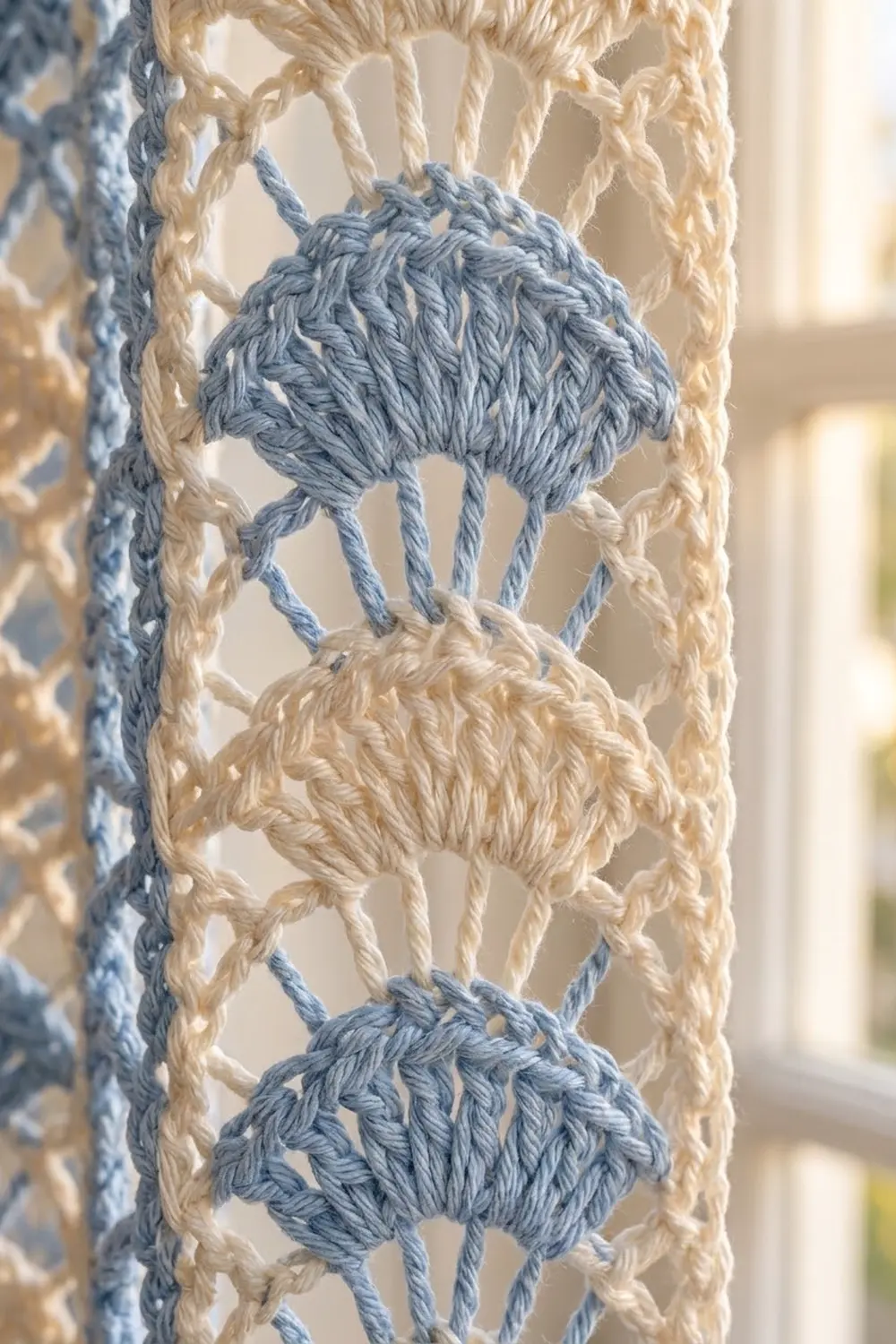 Close-up of decorative crochet trim with blue-gray and cream pompoms alternating on a natural braided base.