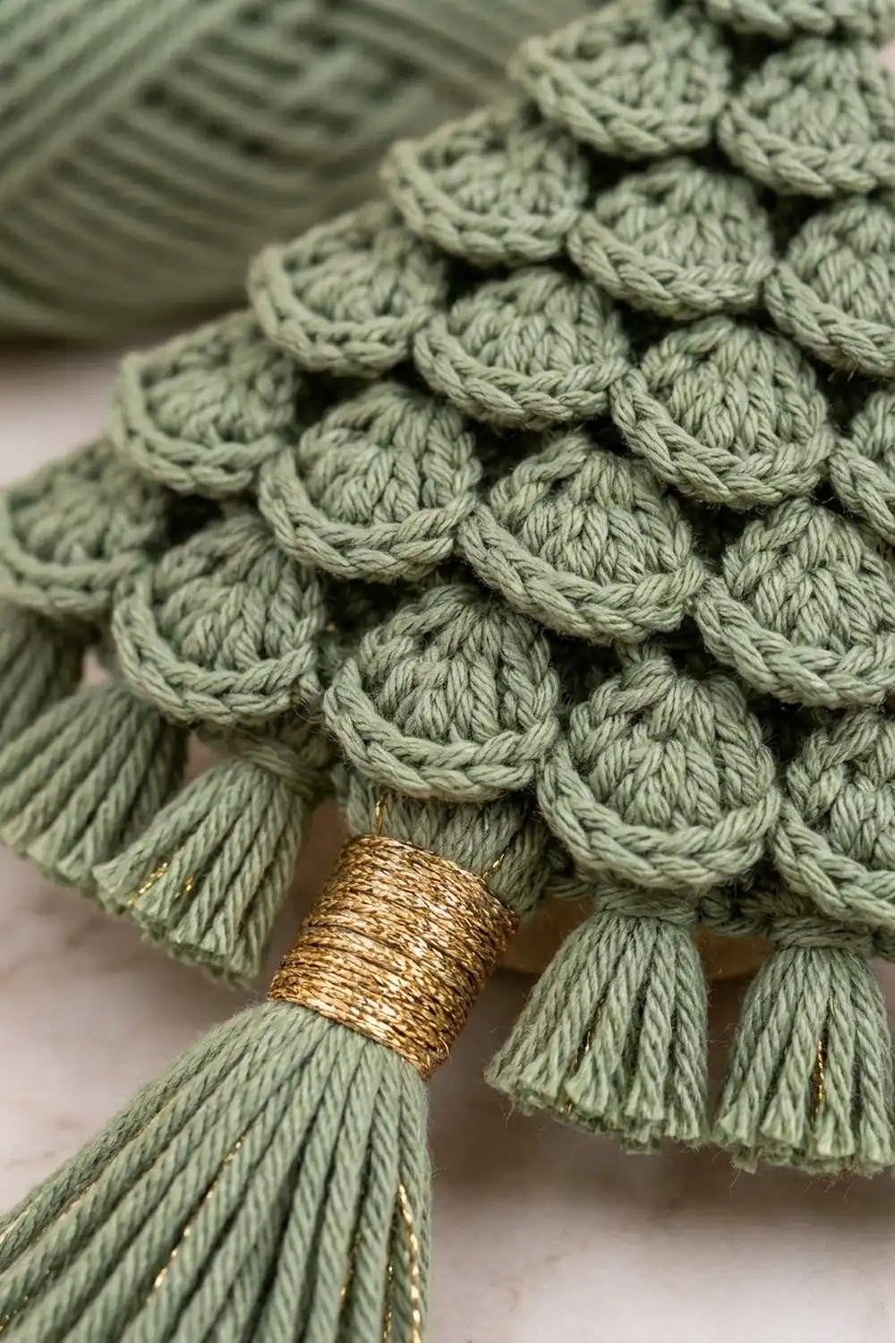 Close-up of sage green crocheted scallop stitch edging with gold-wrapped tassel fringe detail.