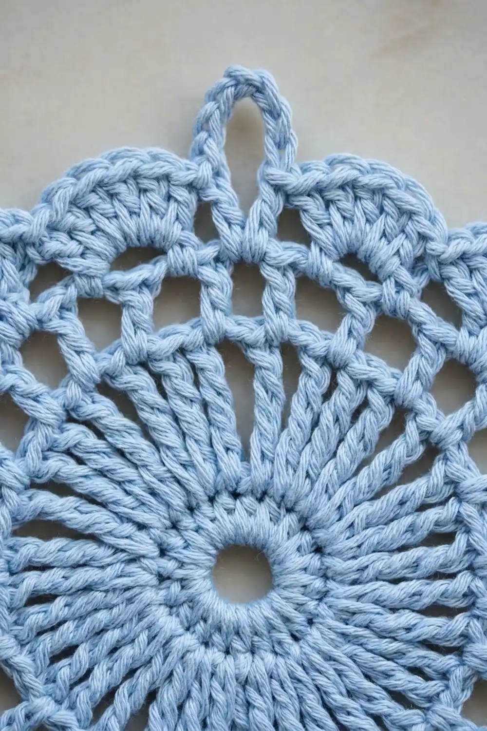 Close-up of a light blue crocheted star ornament with twisted rope texture on a cream background.