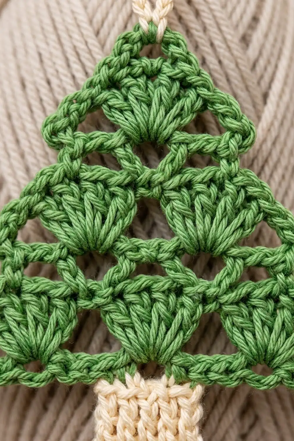 Bright green crocheted triangle with geometric mesh pattern and cream yarn trim displayed on neutral beige fabric.