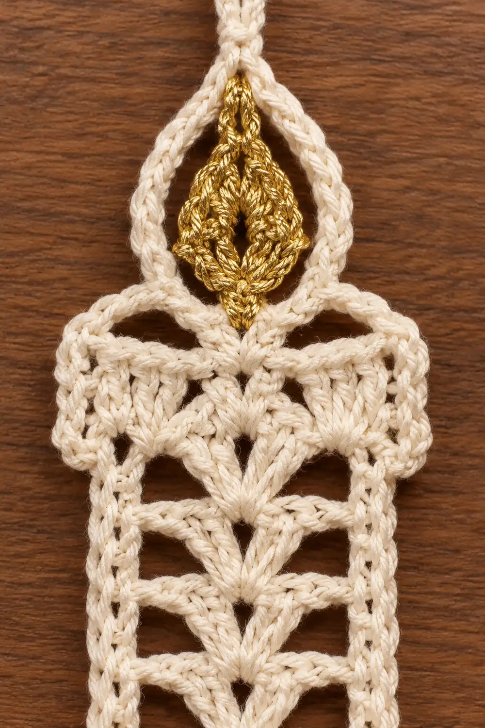 A cream-colored macramé wall hanging with a gold teardrop ornament on a wooden background.