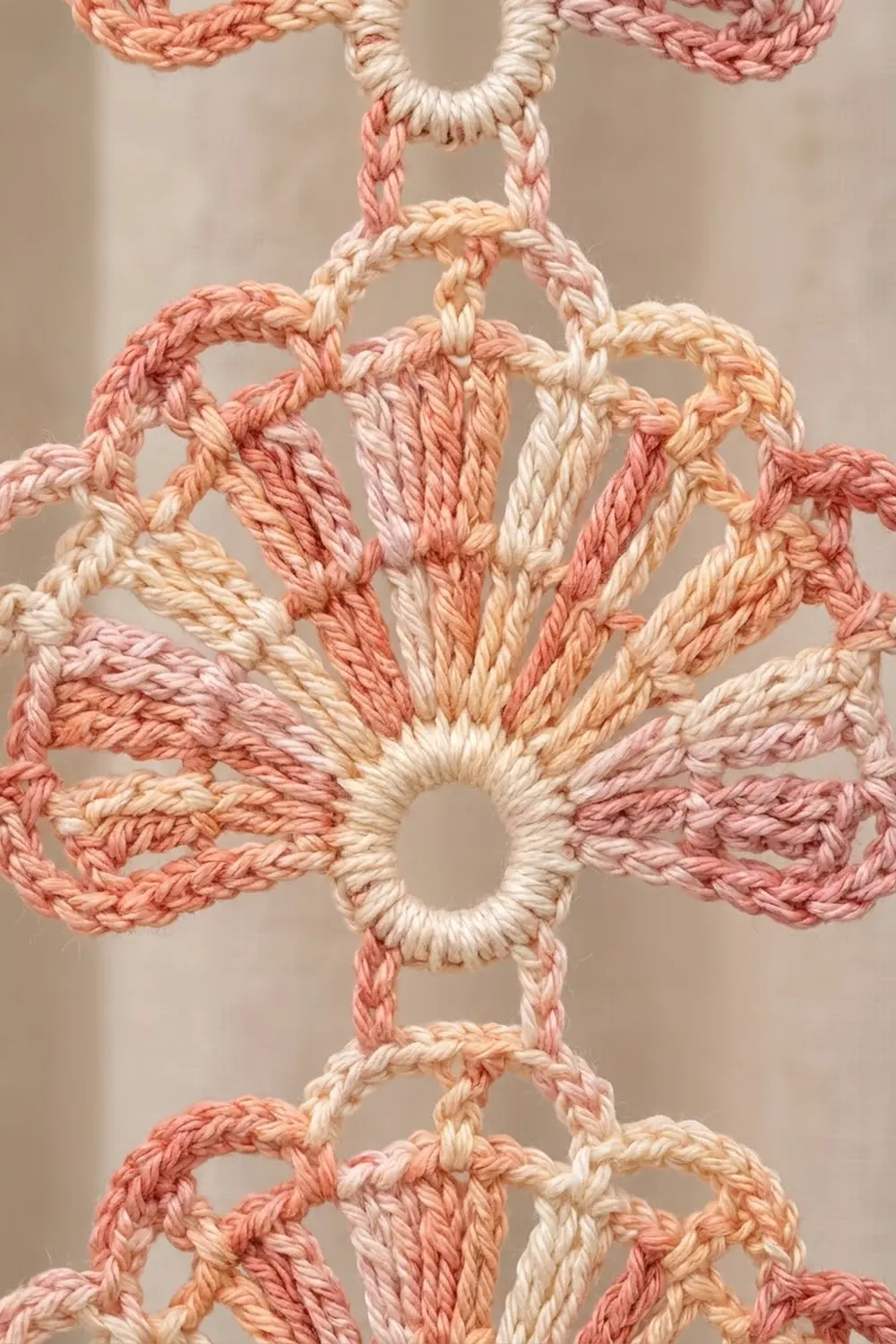 Close-up of crocheted coral, cream, and peach yarn in a symmetrical geometric pattern against a neutral background.