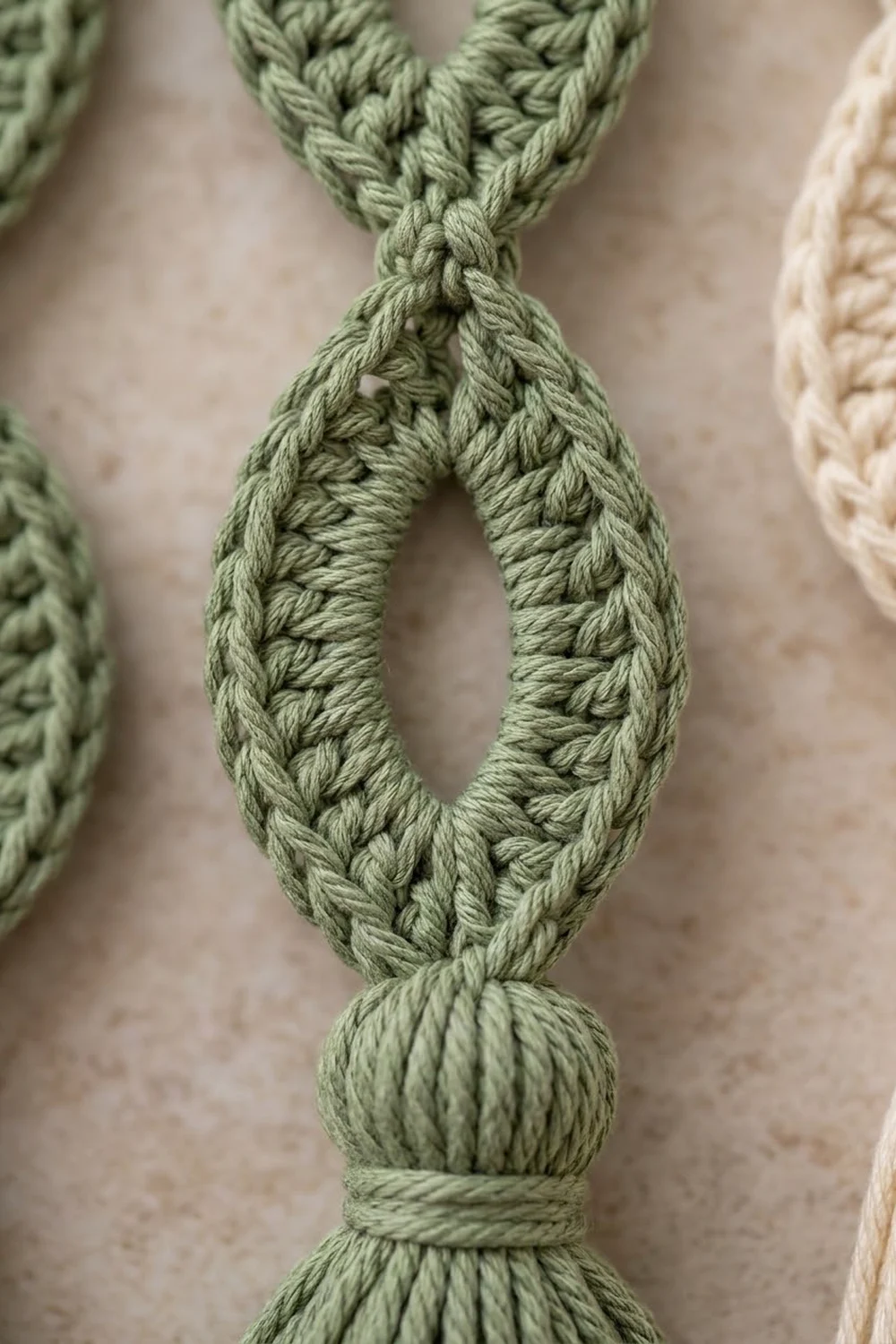 A sage-green crocheted cord tied in a decorative loop with intricate stitching detail against neutral background.