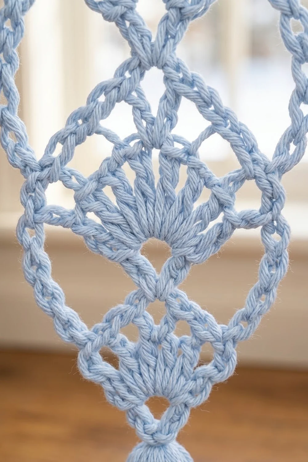 Close-up of light blue crochet lace displaying intricate diamond and geometric motifs with visible yarn texture and knots.