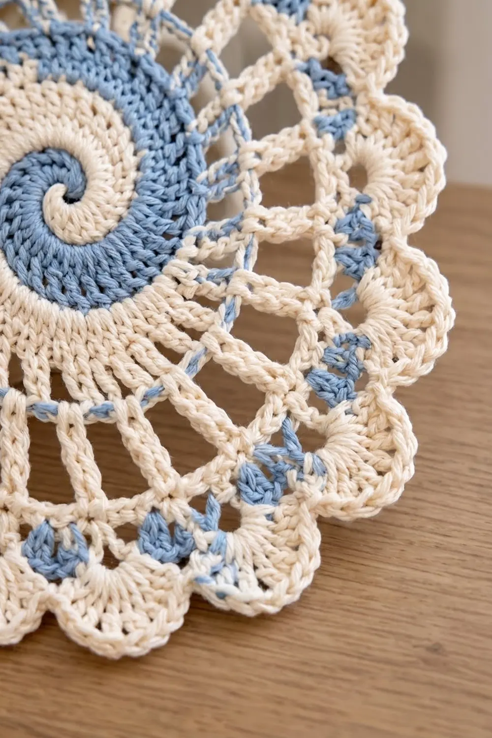 Close-up of intricate blue and cream crocheted lace with openwork patterns and scrolled detail on a wooden surface.