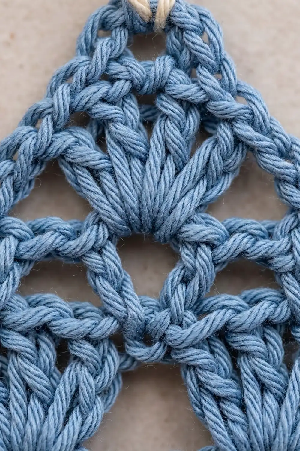 Blue twisted yarn forms an interlocking knotted lattice pattern against a neutral beige background.