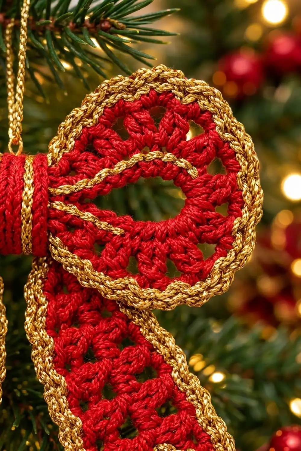 Red crocheted snowflake ornament with gold metallic trim, hung on an evergreen branch amid blurred Christmas decorations.