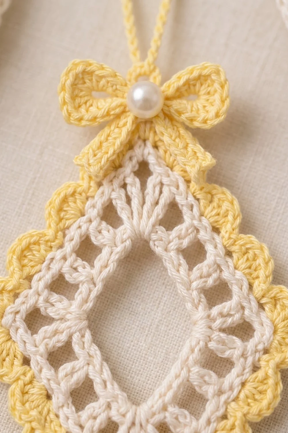 Crocheted Christmas tree ornament with golden yellow bow, white pearl bead, and cream lacy tree outlined in yellow crochet trim.