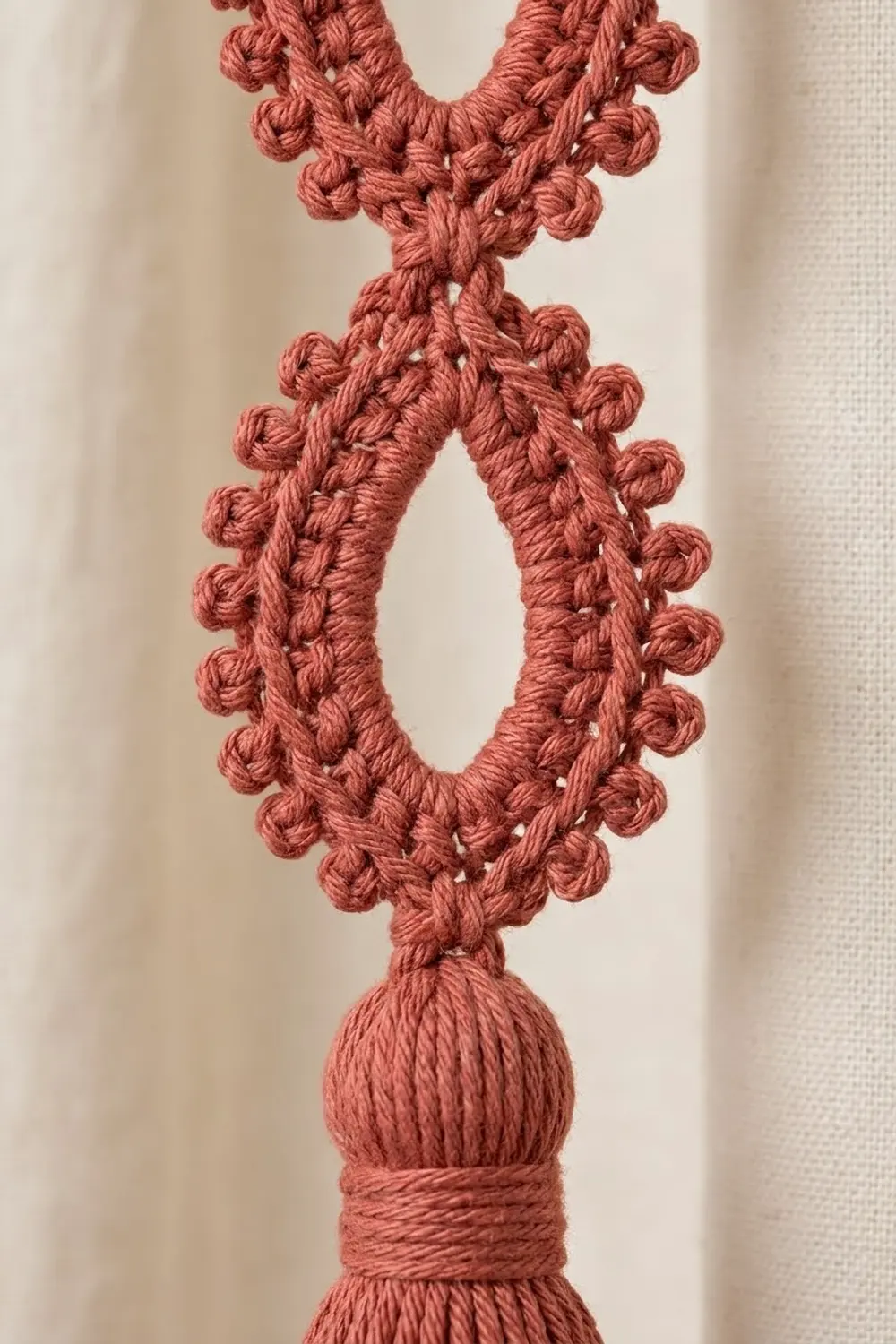 Crocheted terra cotta yarn pendant featuring a diamond shape edged with decorative bobbles and a tassel base.